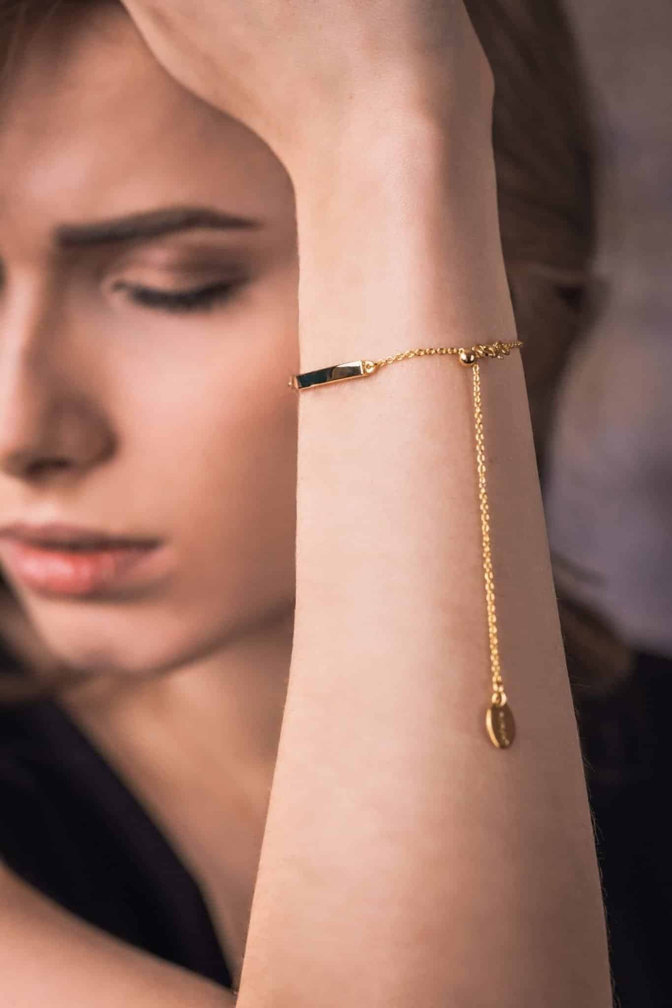 Gliederkettenarmband aus Gold mit einem rechteckigen schwarzen Anhänger und einem kleinen ovalen Anhänger.