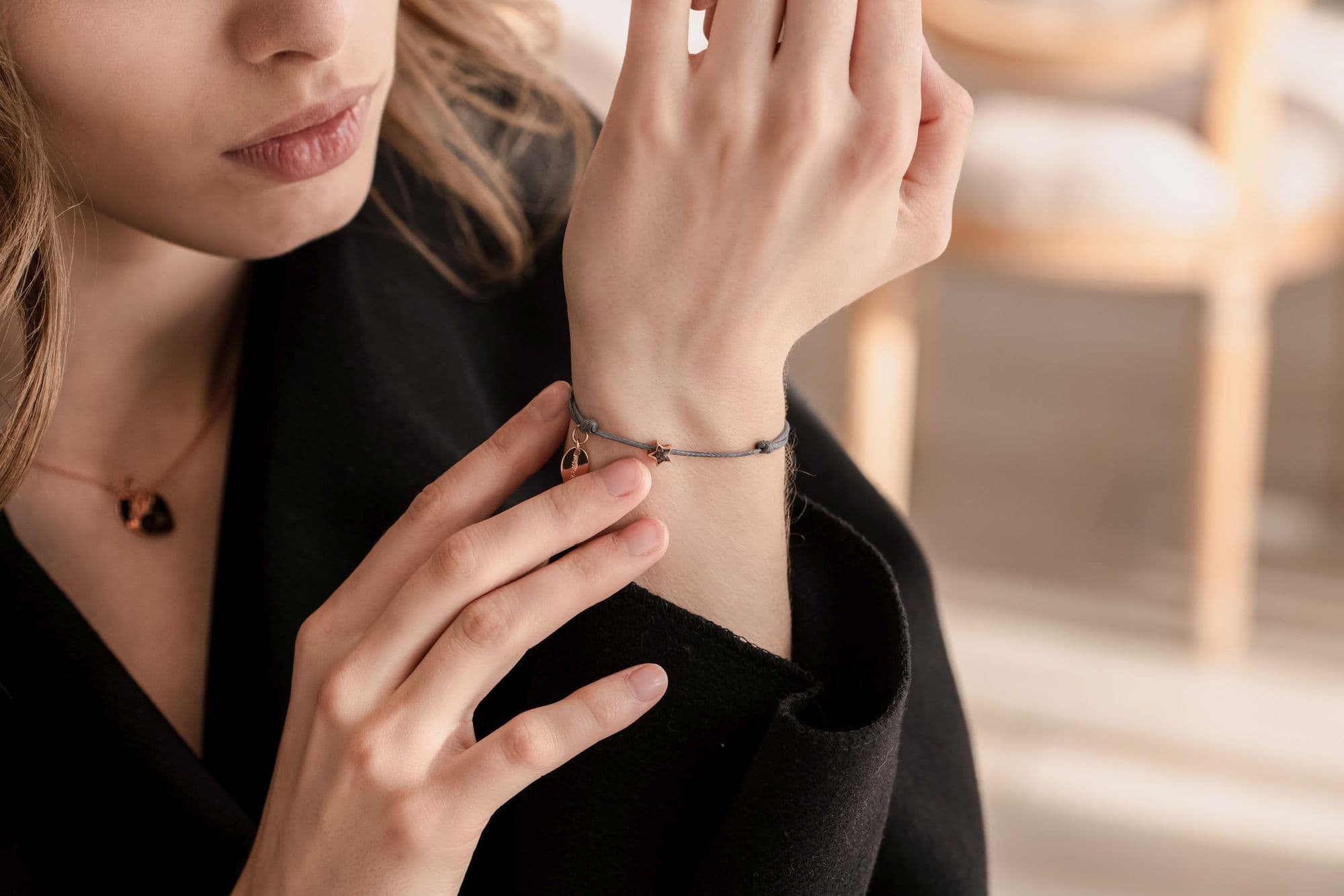 Graues Kordelarmband mit einem roségoldenen Stern und einem ovalen Anhänger.