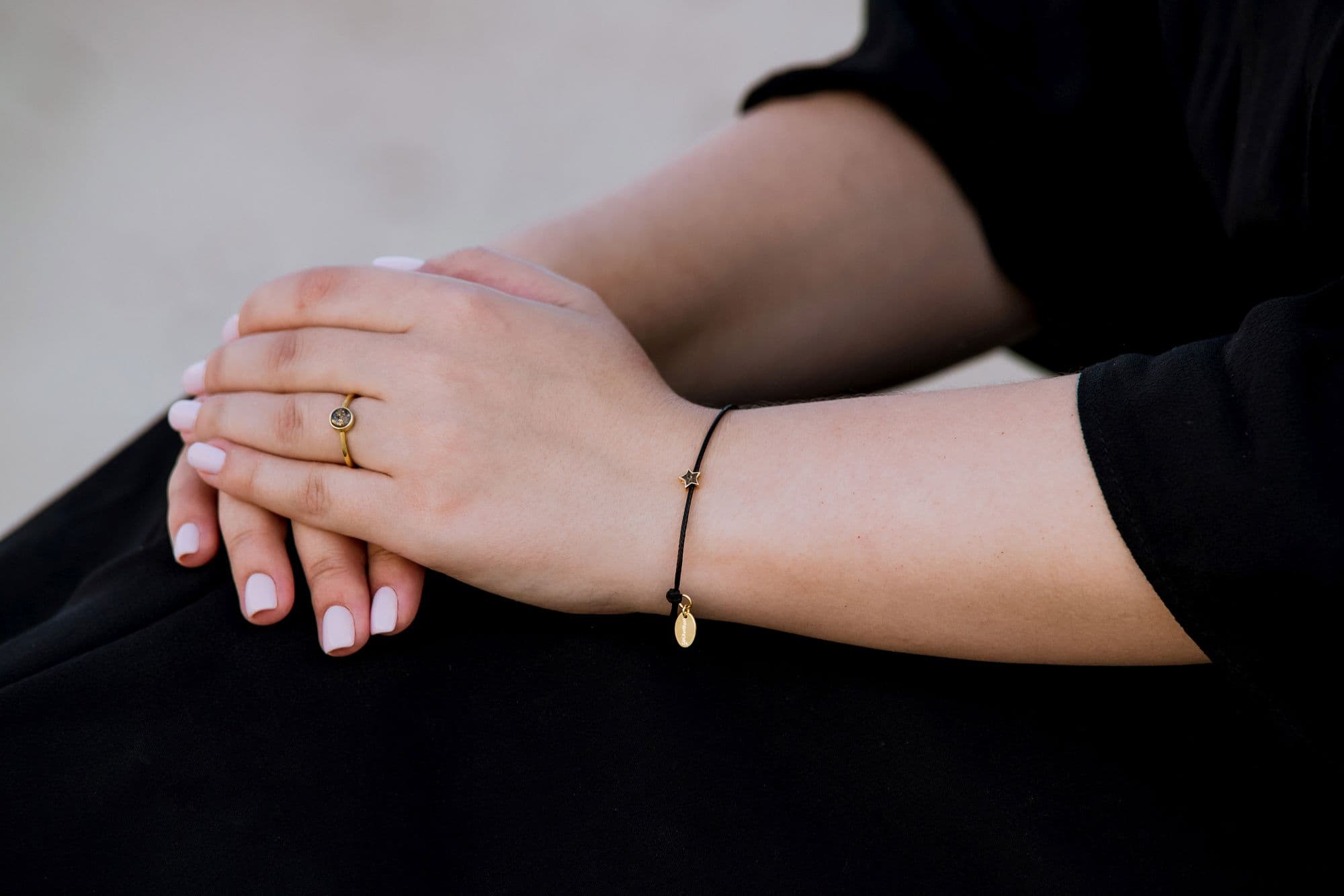 Goldring mit einem runden, gesprenkelten Stein und ein schwarzes Kordelarmband mit einem goldenen Sternanhänger und einer ovalen Plakette.