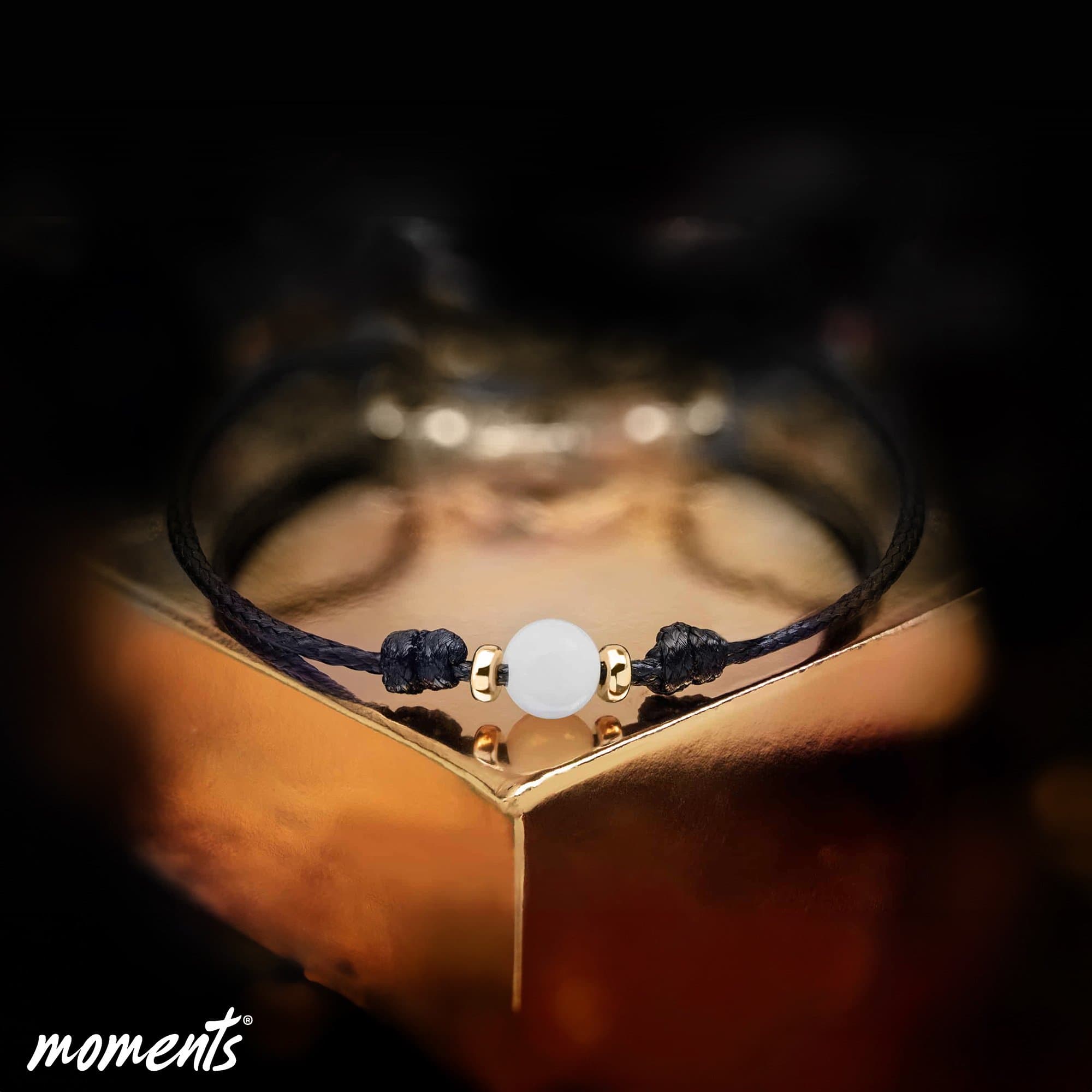 Schwarzes Kordelarmband mit einer weißen Perle und goldenen Akzenten.