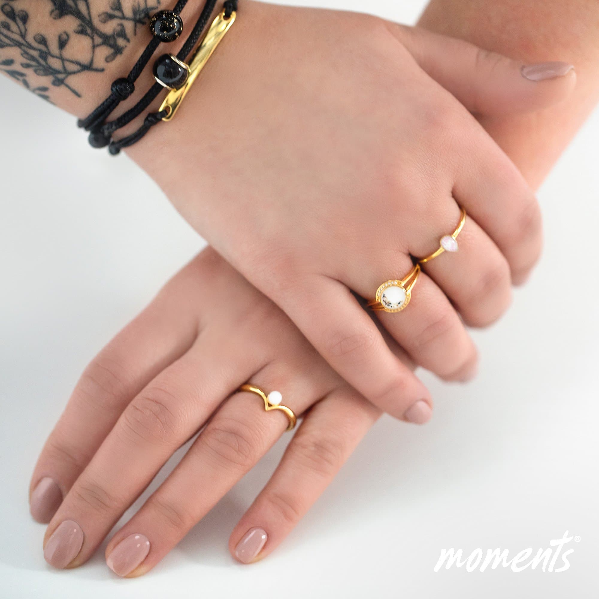 Goldring mit einem weißen ovalen Stein und schwarzen Sprenkeln, sowie ein goldener Chevron-Ring mit einer weißen Perle.