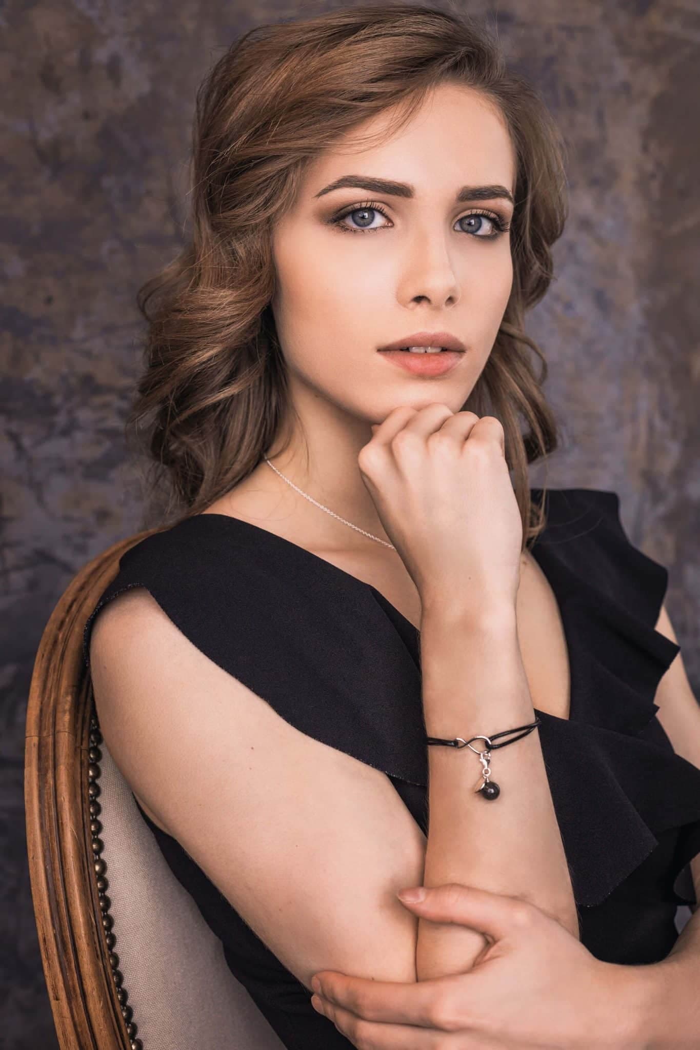 Schwarzes Kordelarmband mit einem silbernen Unendlichkeitsanhänger und einem dunklen, runden Anhänger.