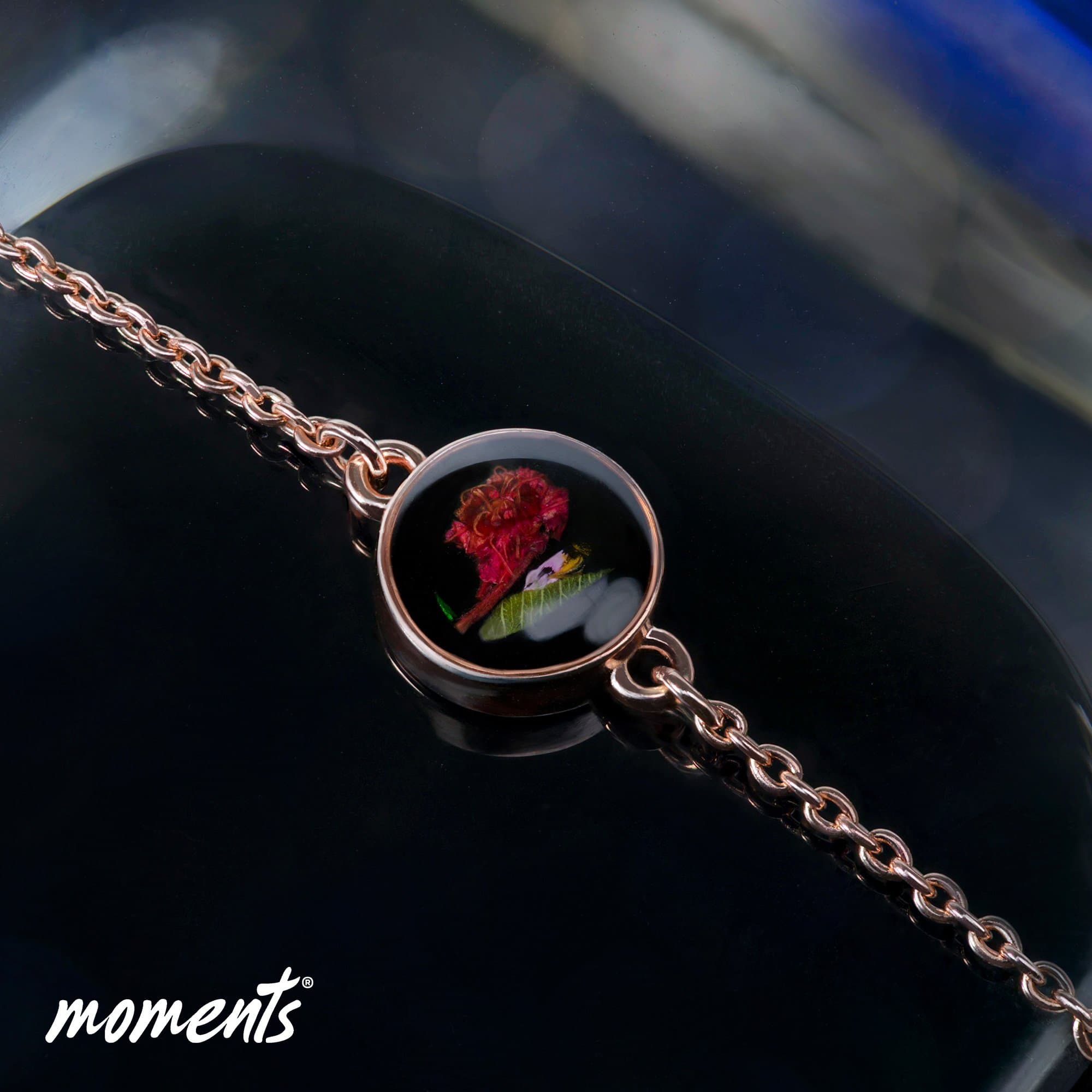 Roségoldenes Kettenarmband mit einem runden Medaillon, das eine rote Blume und grüne Blätter enthält.