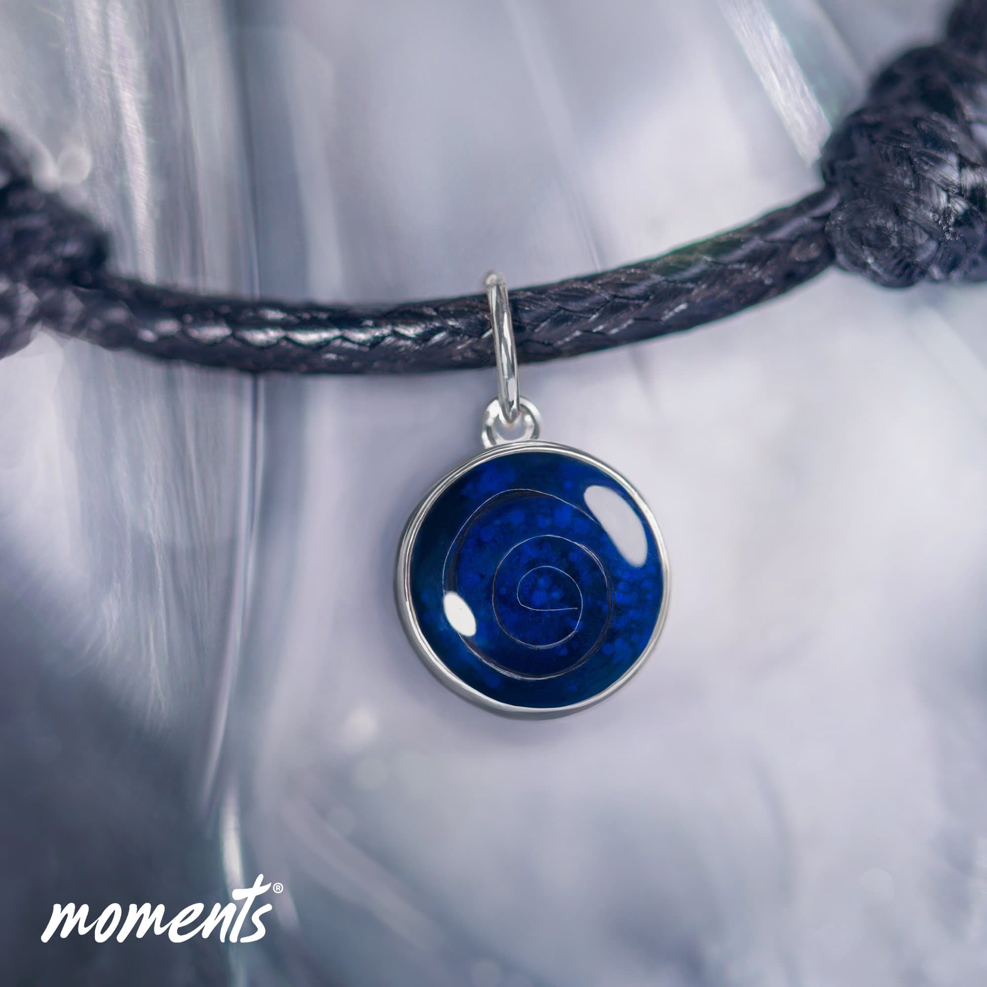 Silberner Anhänger mit einem blauen Spiraldesign an einer schwarzen Kordel.
