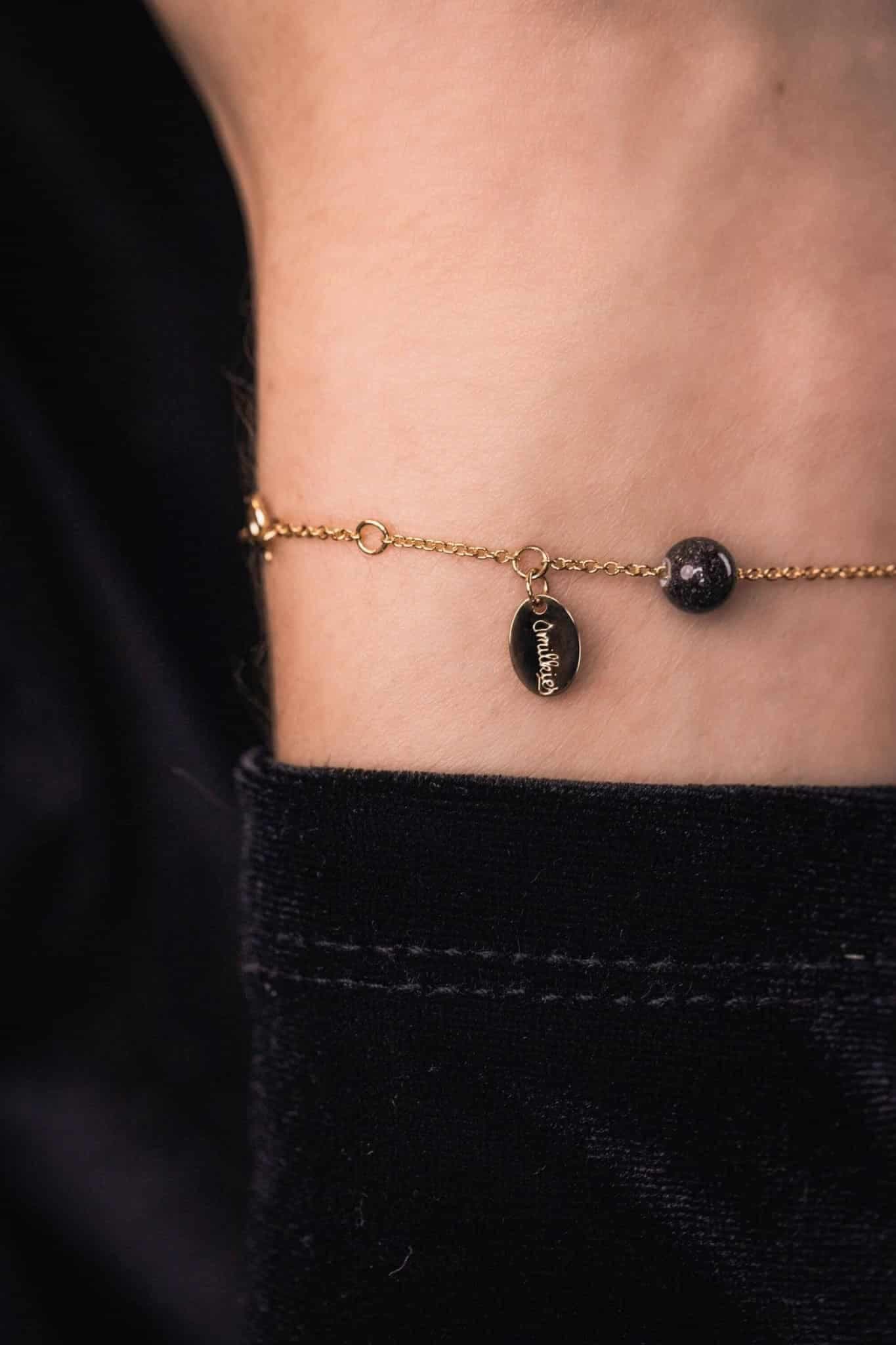 Goldfarbenes Armband mit einem ovalen Anhänger und einer dunklen, gesprenkelten Perle.