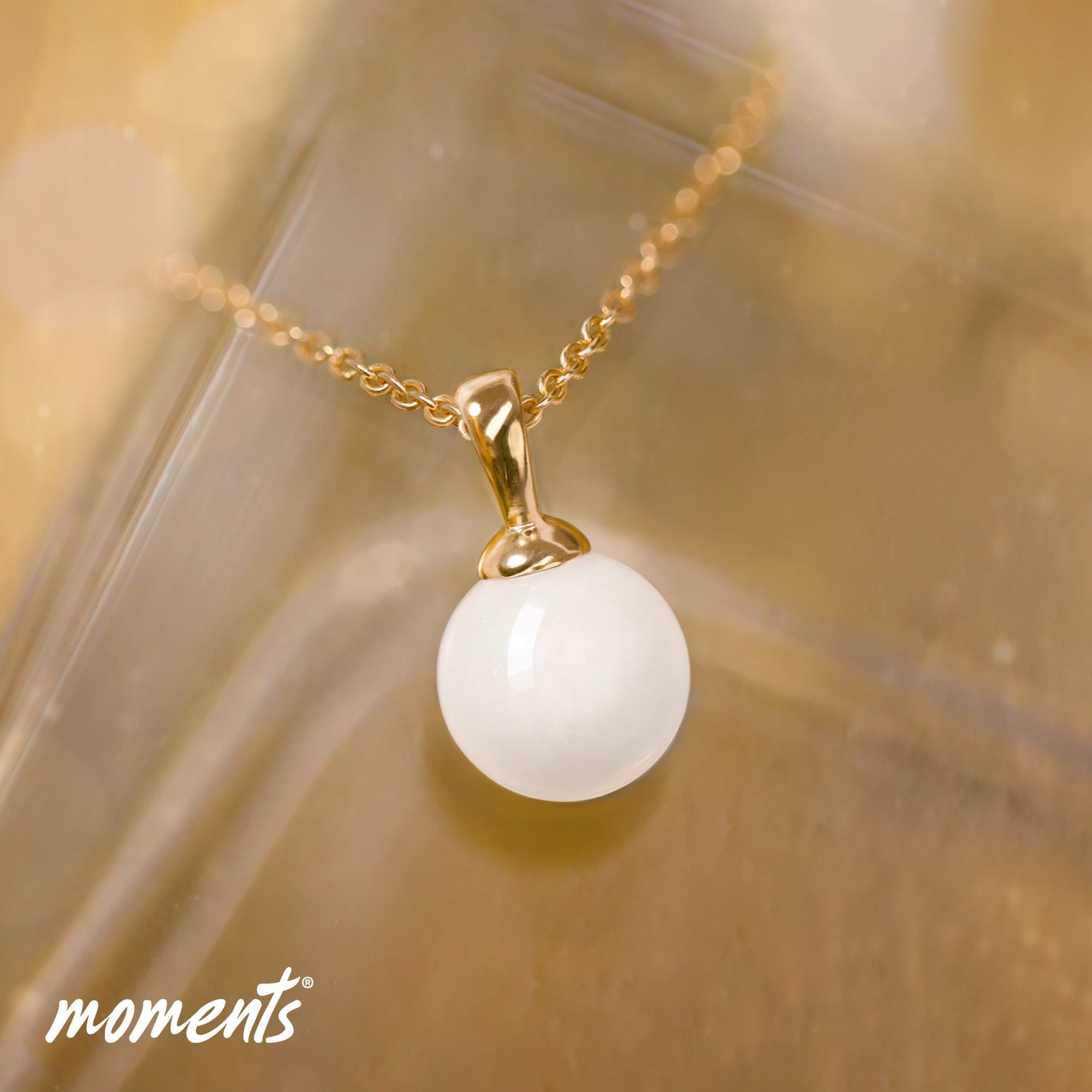 Goldgliederkette mit einem glatten, weißen, kugelförmigen Anhänger.