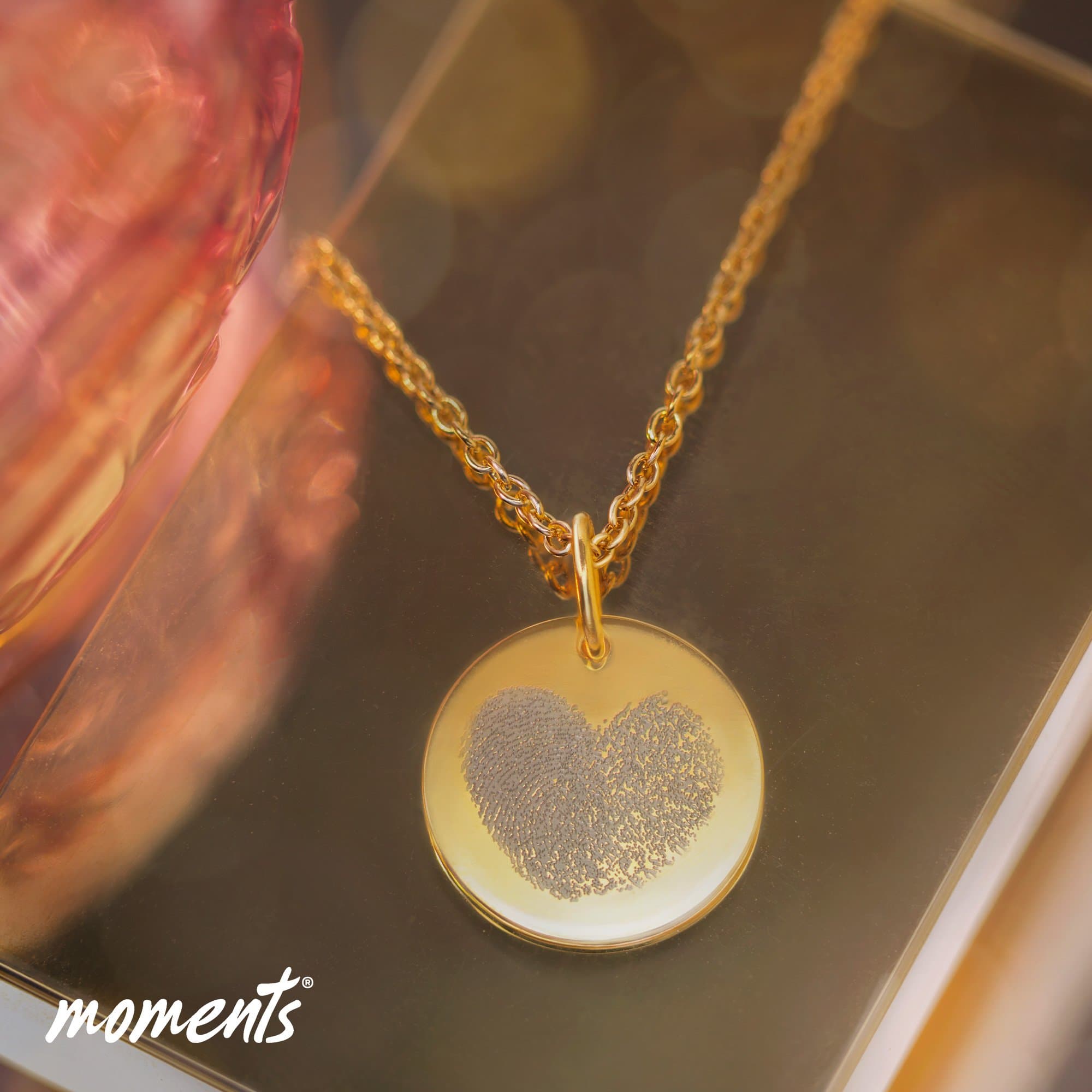 Goldene Halskette mit rundem Anhänger, der eine herzförmige Fingerabdruck-Gravur aufweist.
