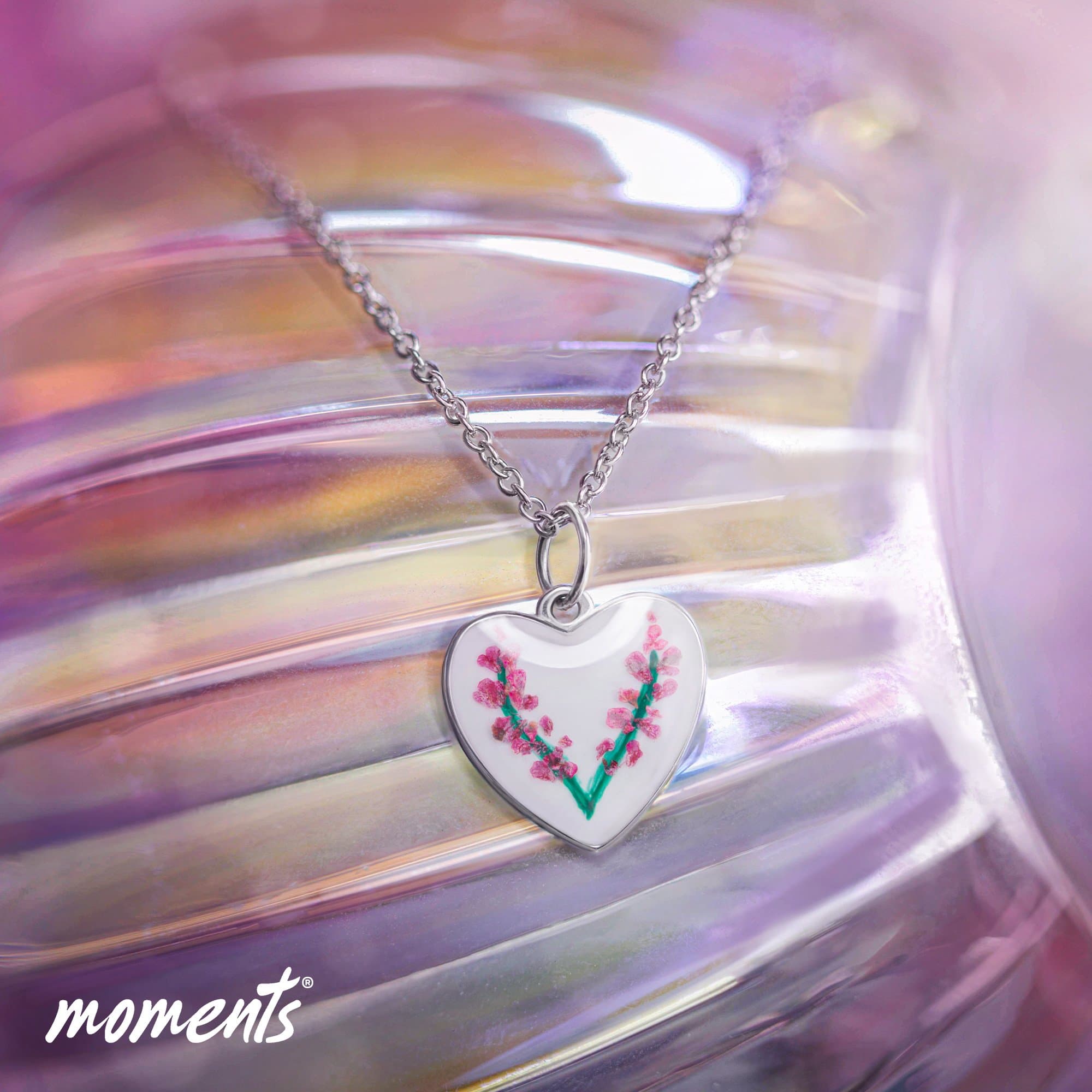 Silberner Herzanhänger mit weißer Emaille und rosa Blumendesign an einer silbernen Kette.