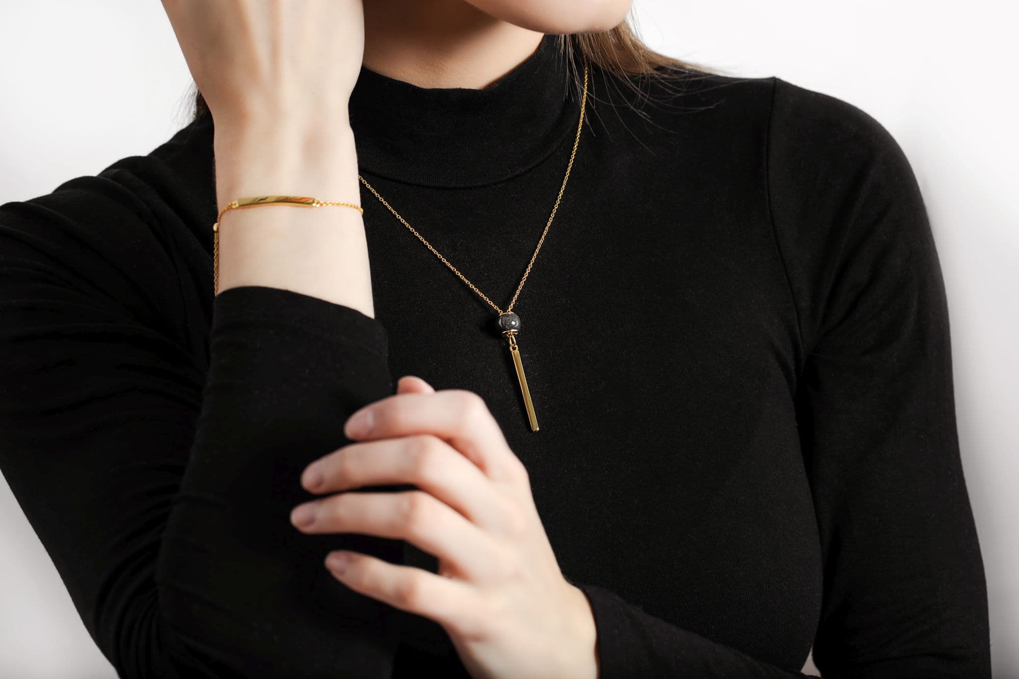 Goldenes Barrenarmband und goldene Halskette mit einer dunkelgrauen Perle und goldenem Barrenanhänger.