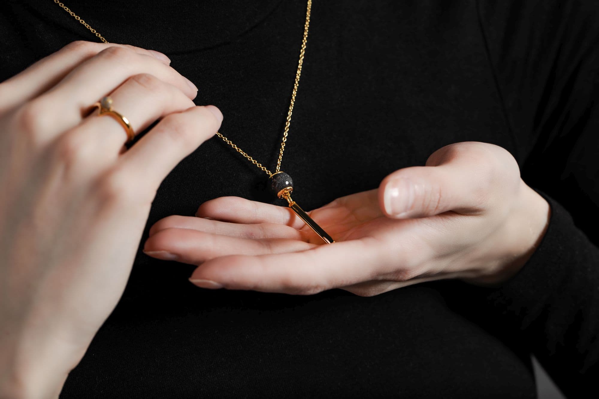 Goldene Halskette mit einer dunkelgrauen gesprenkelten Perle und einem goldenen Barrenanhänger.
