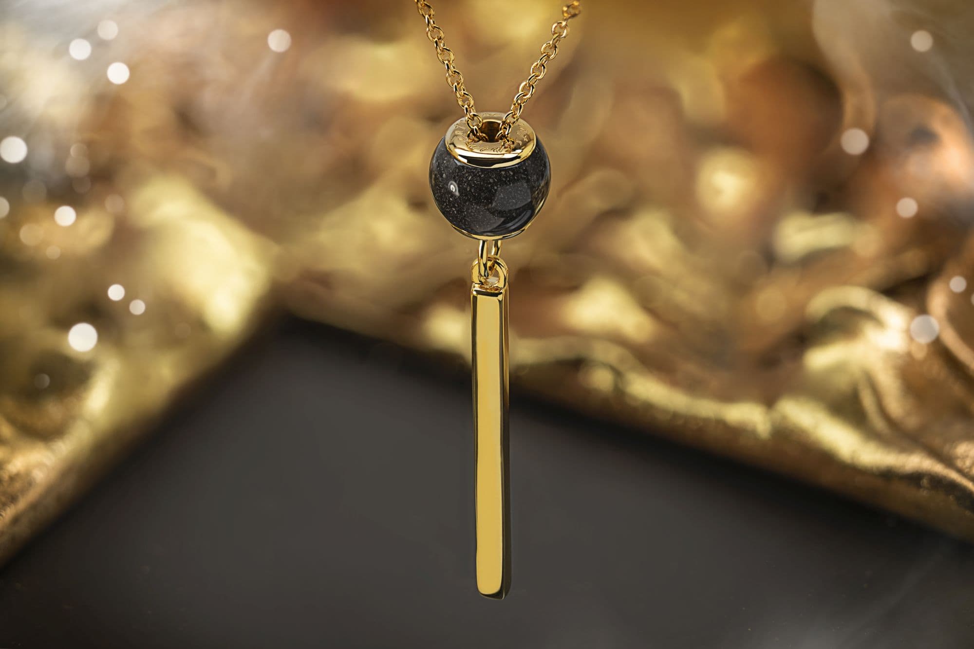 Goldene Halskette mit einer schwarz gesprenkelten Perle und einem goldenen Barrenanhänger.