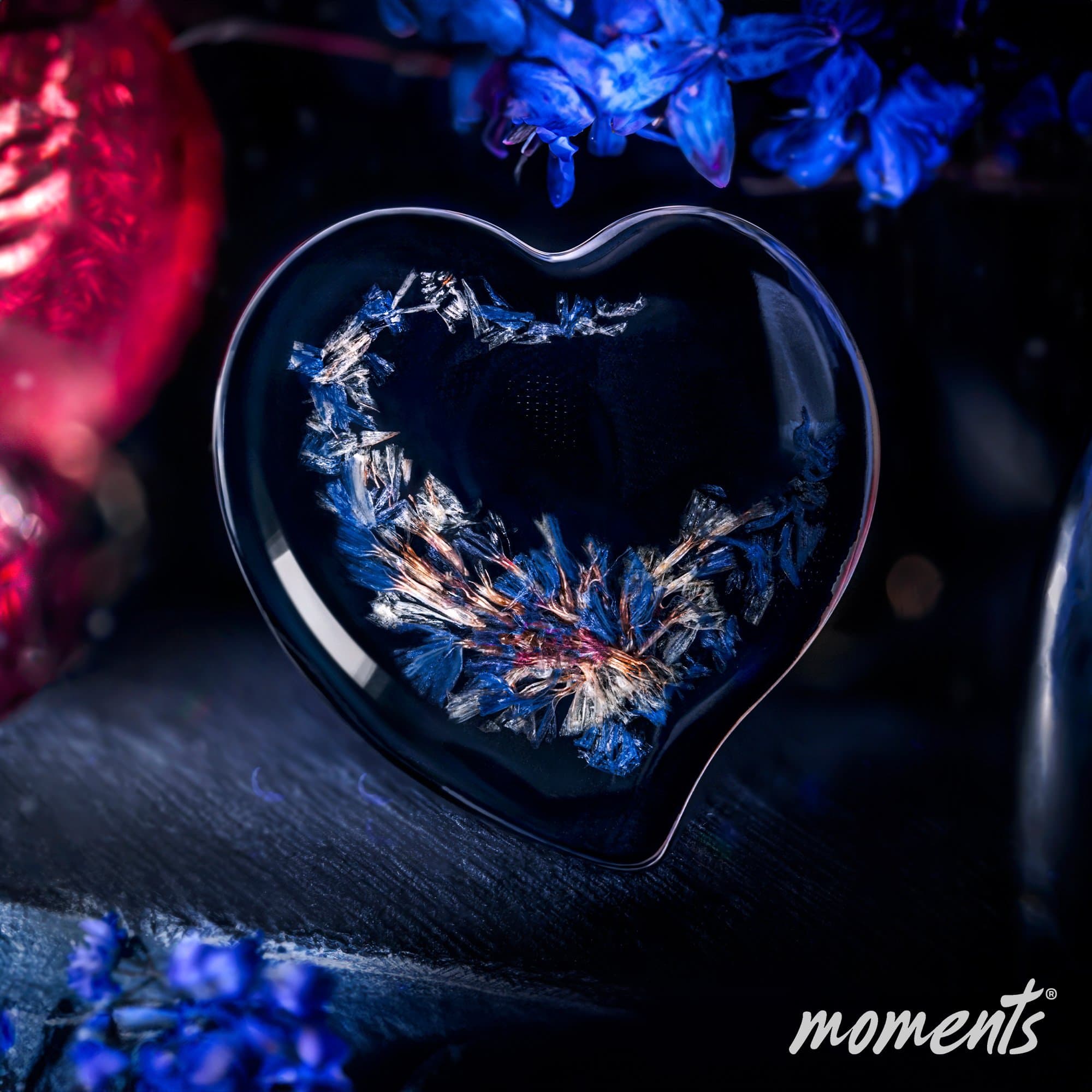 Herzförmiges Glas-Andenken mit eingebetteten blauen und weißen floralen Elementen.