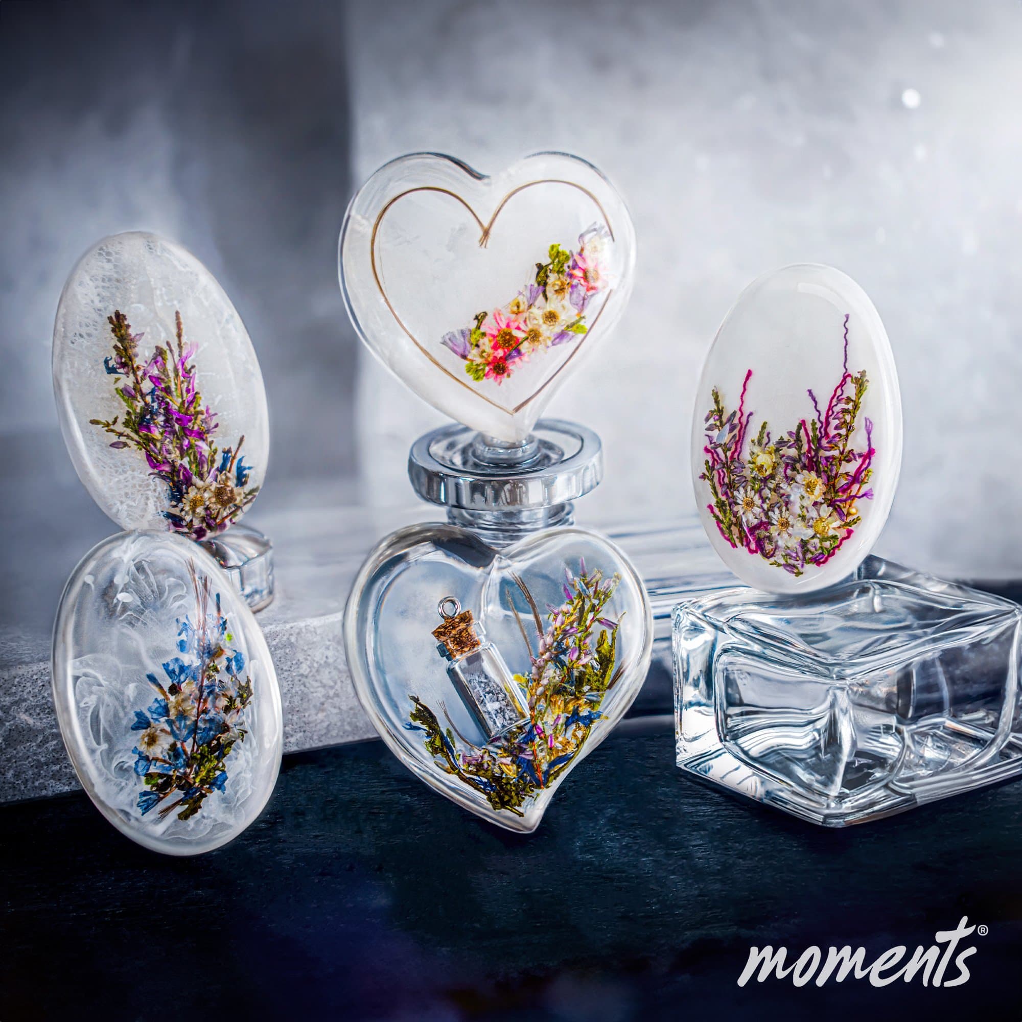 Ovaler und herzförmiger Harzschmuck mit eingebetteten getrockneten Blumen in weißen, blauen und rosa Farbtönen.
