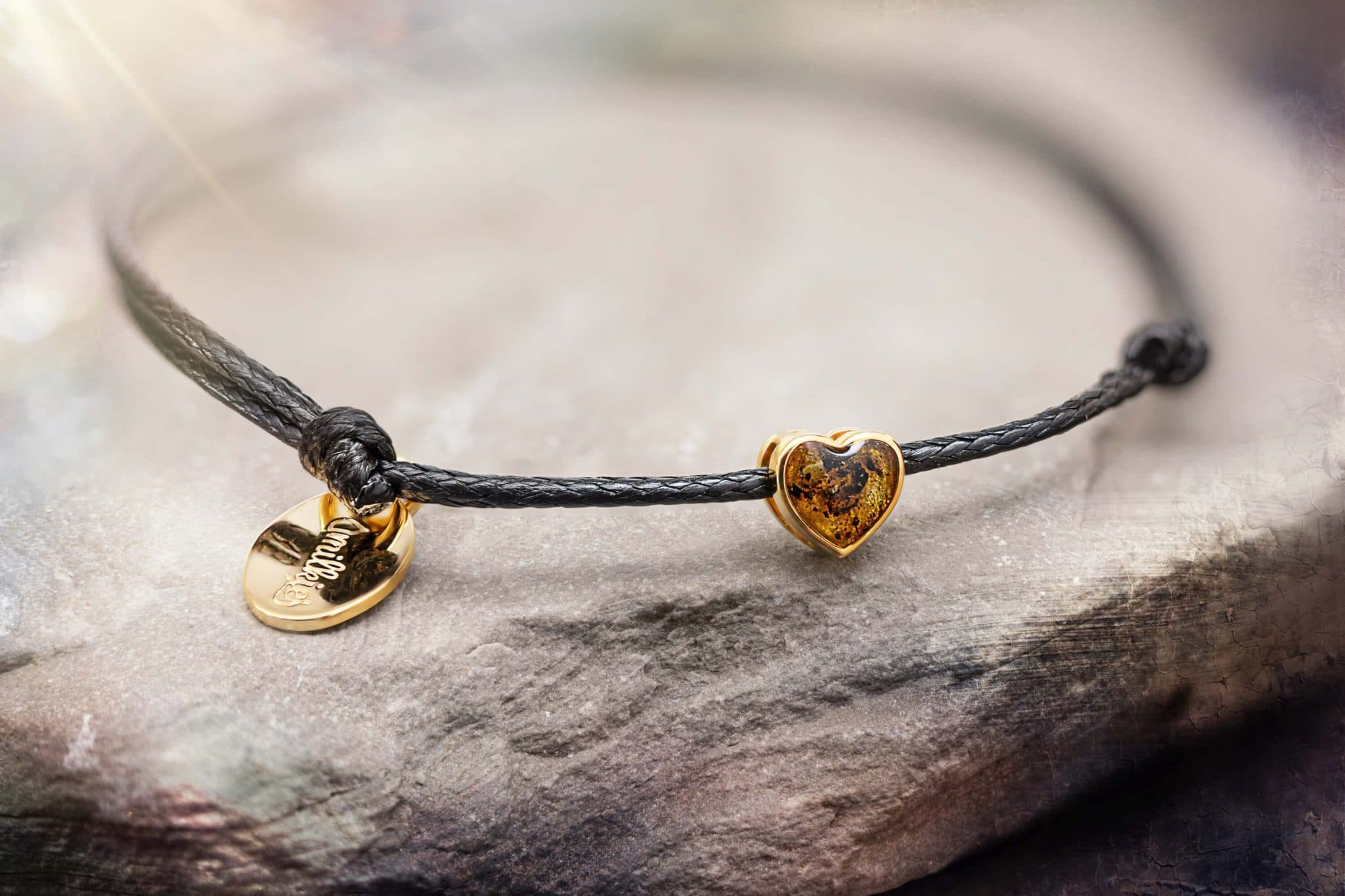 Armband mit schwarzem Band, einem goldenen herzförmigen Bernstein-Charm und einem ovalen goldenen Anhänger.