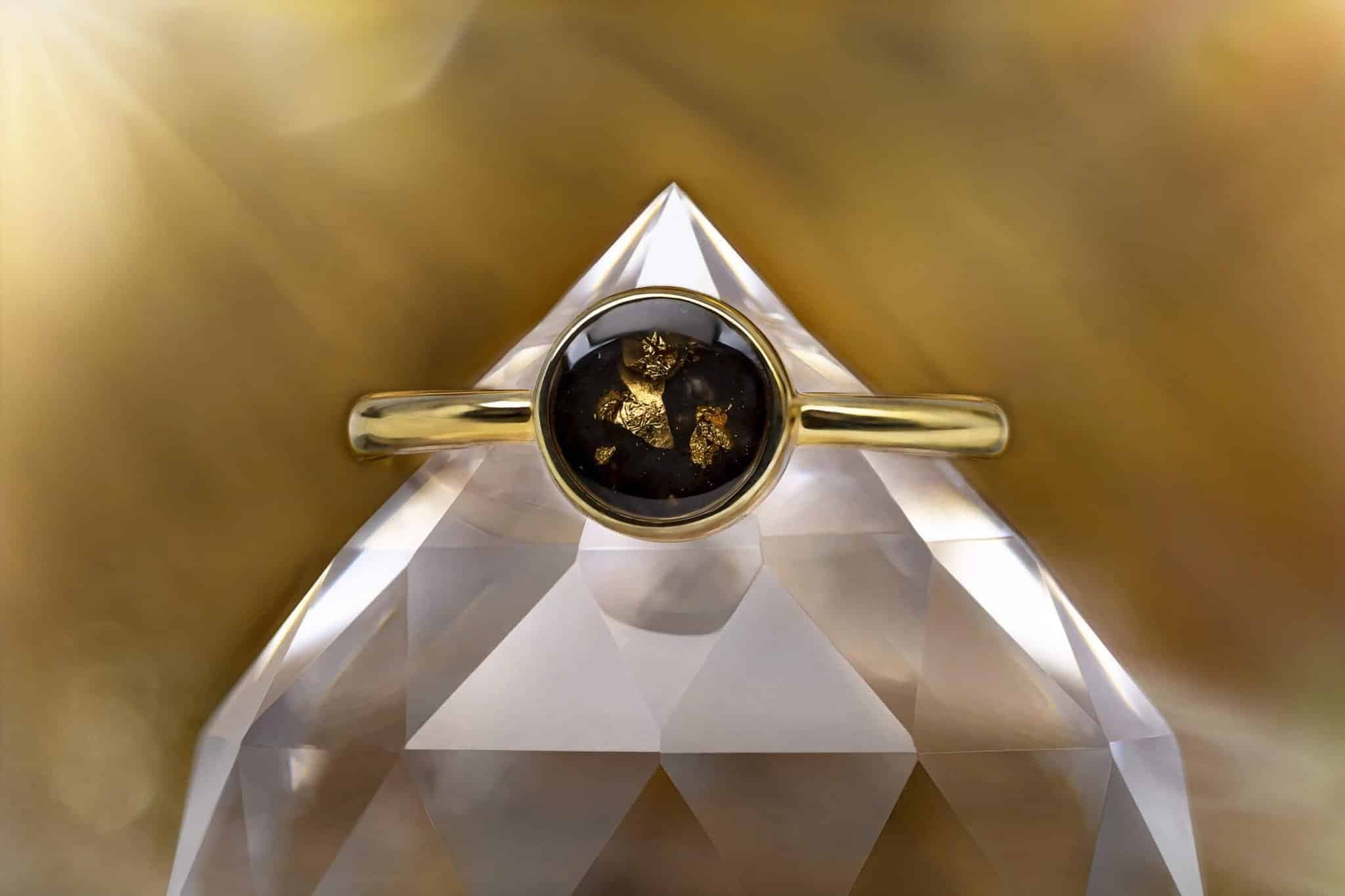 Goldring mit einem runden, dunklen Cabochon, der Blattgoldfragmente enthält.