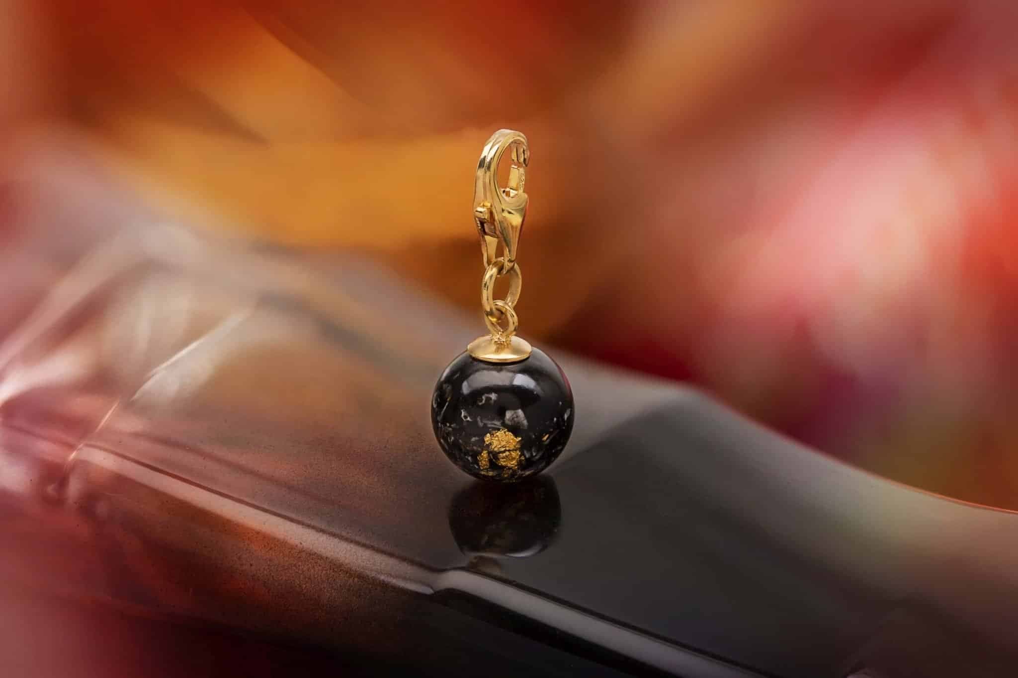 Vergoldeter Charm mit einer schwarzen Kugel, die Goldflecken enthält.