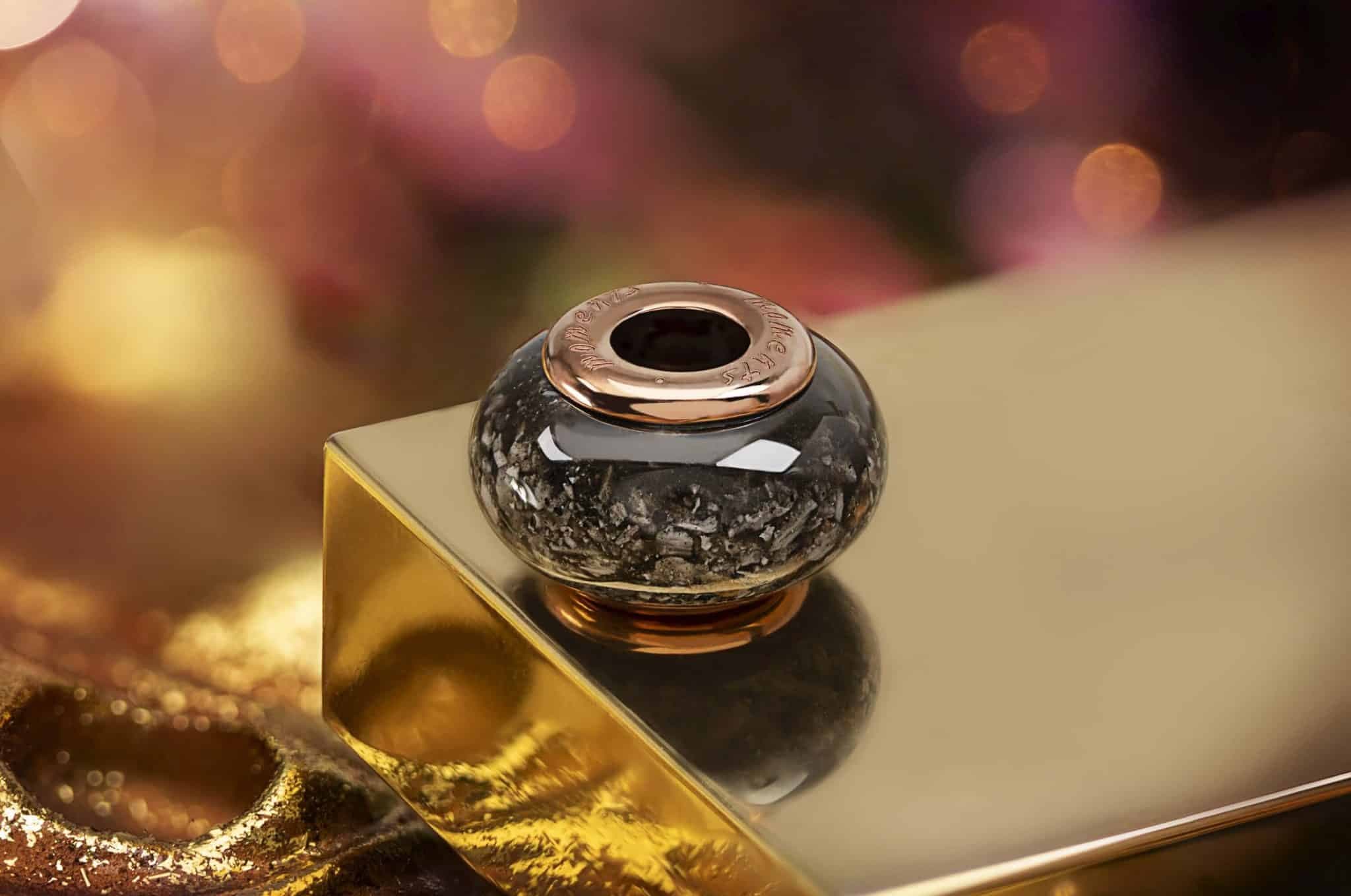 Runde schwarze Erinnerungsperle mit roségoldfarbenem Rand, die sichtbare Aschefragmente enthält.