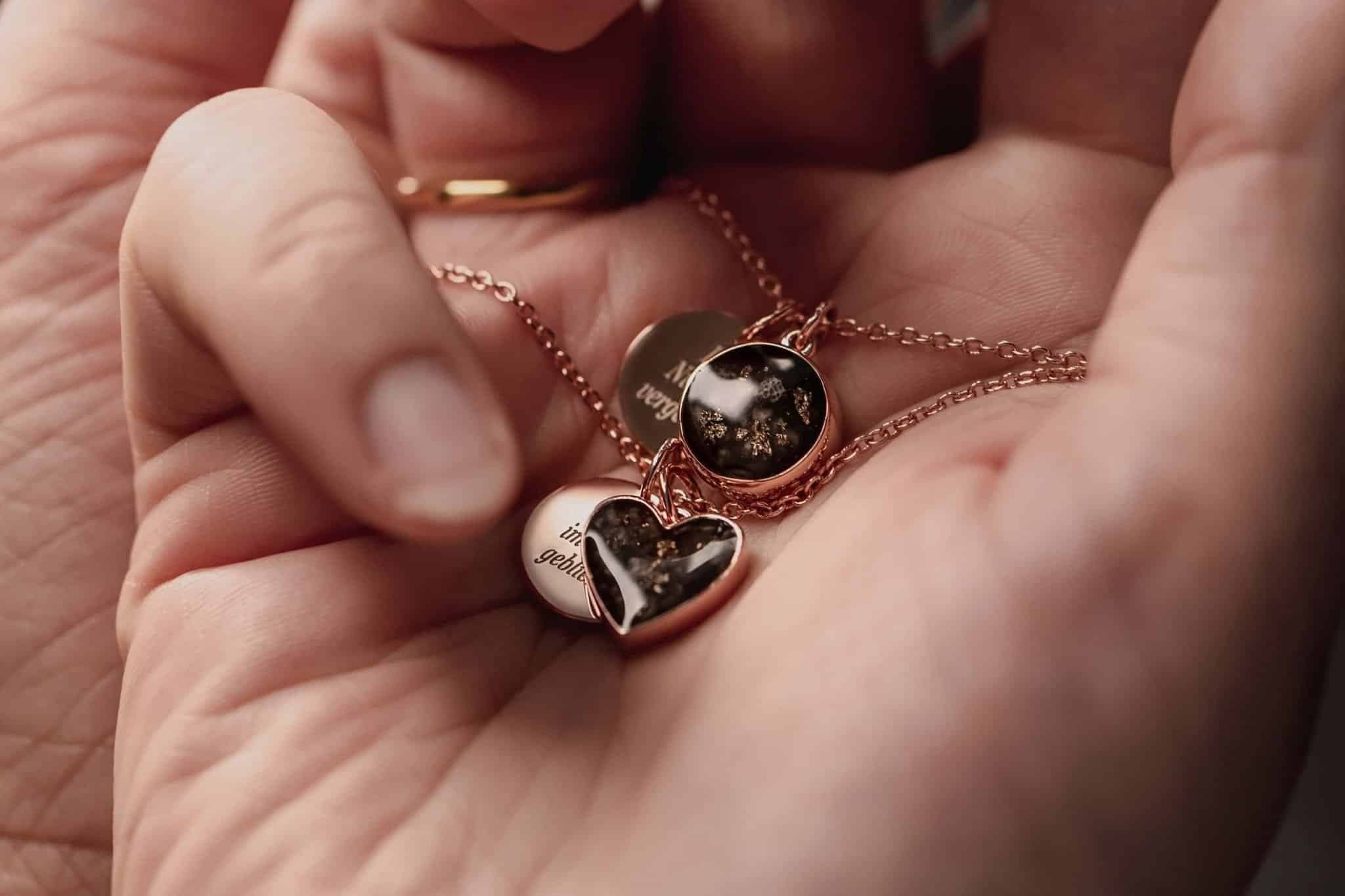 Roségoldfarbene Halskette mit einem herzförmigen Anhänger und einem runden Anhänger, beide mit dunklem Material mit Goldflecken.