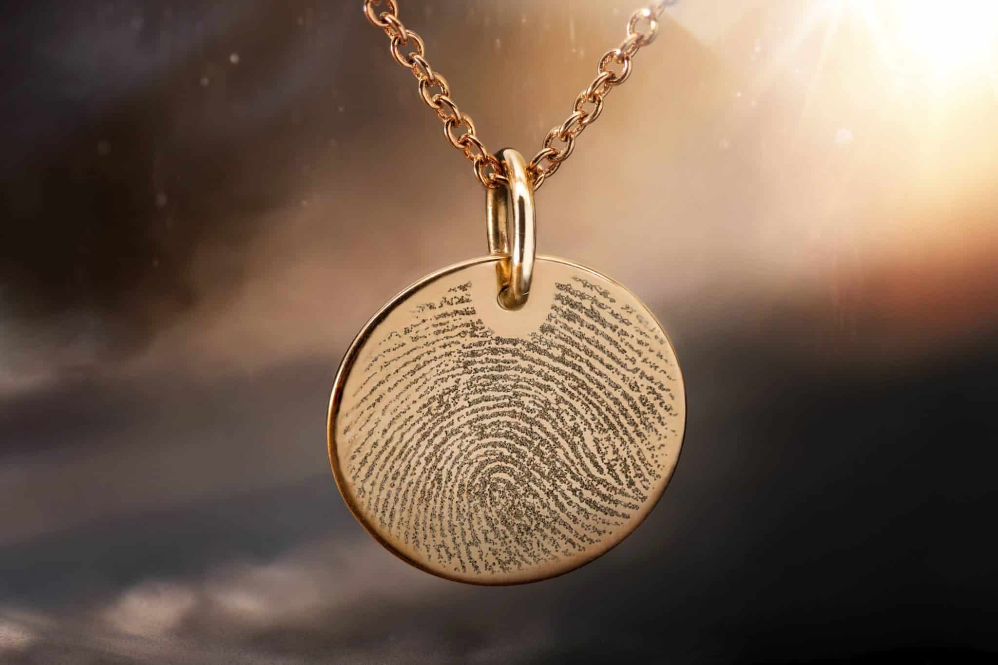 Goldfarbener runder Anhänger mit Fingerabdruckgravur an einer Kette.
