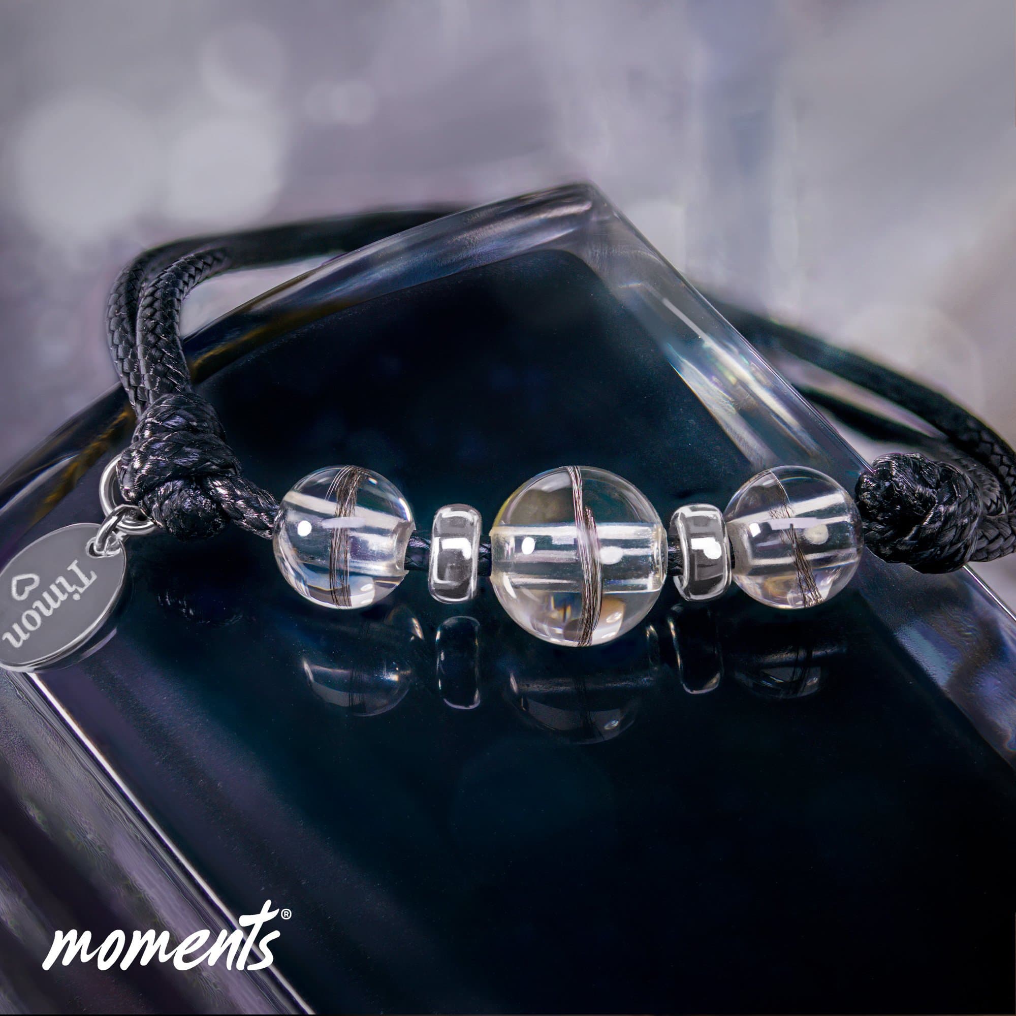 Armband mit schwarzem geflochtenem Band, klaren Glasperlen mit dunklen Strähnen und einem silbernen ovalen Charm.