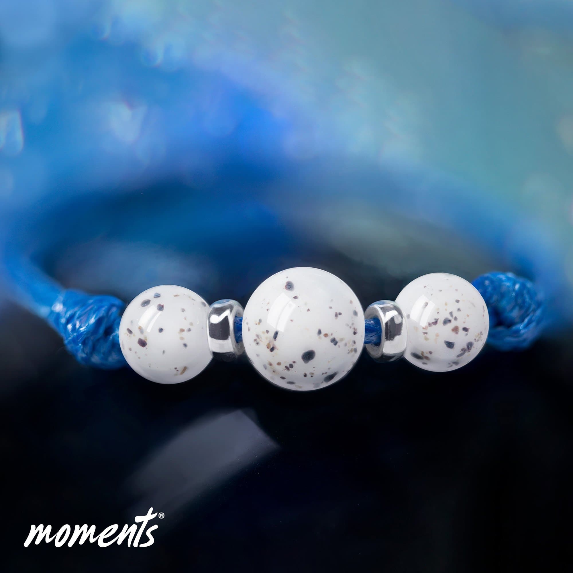 Armband mit blauem Band, drei weißen Perlen mit dunklen Sprenkeln und silbernen Zwischenstücken.