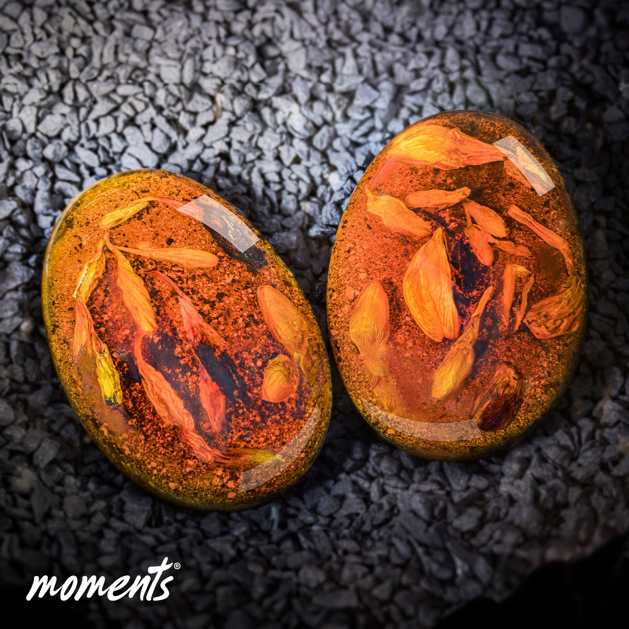 Ovale Erinnerungssteine aus bernsteinfarbenem Harz mit eingeschlossenen orangefarbenen Blütenblättern und dunklen Sprenkeln.