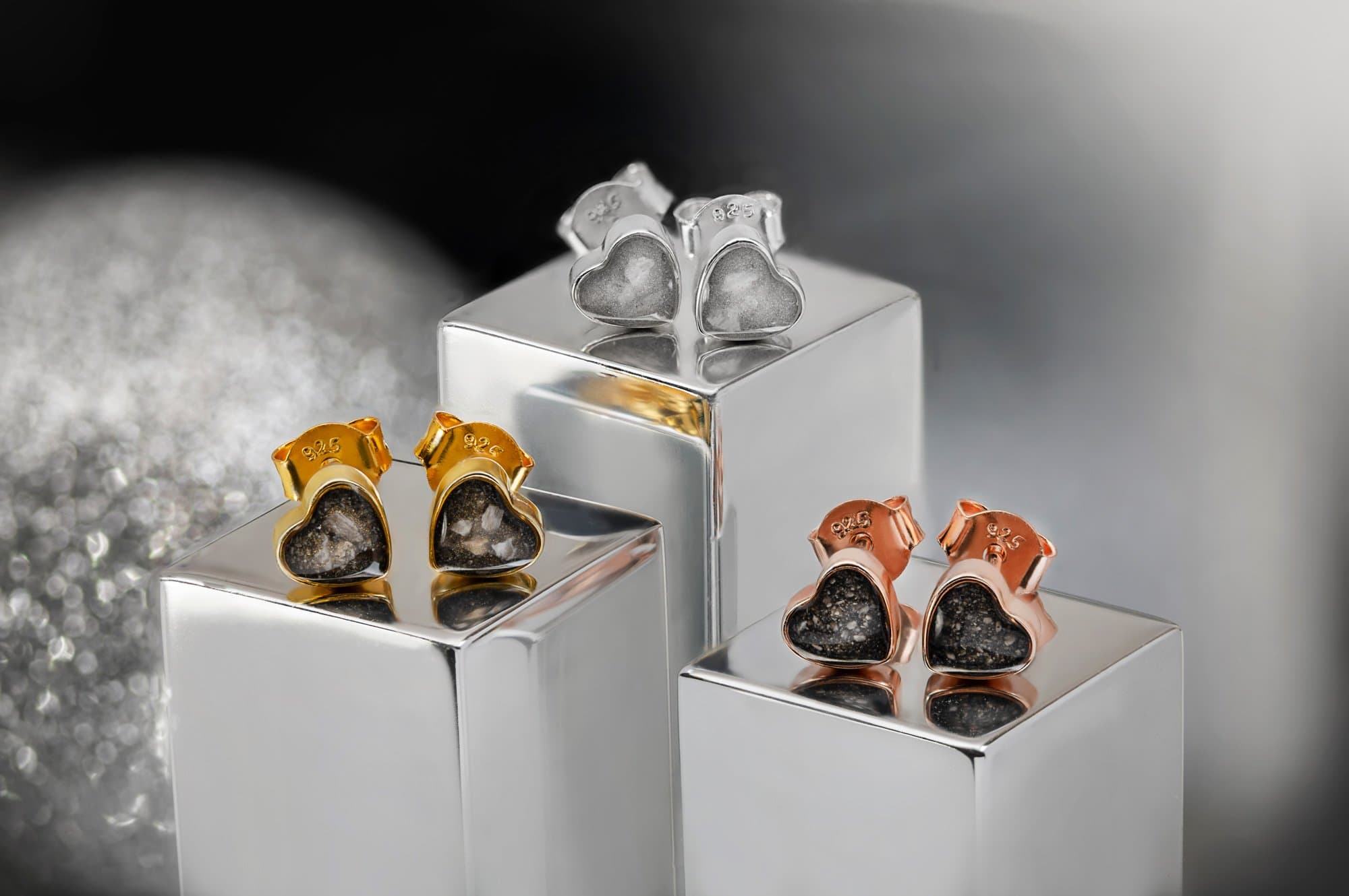 Herzförmige Ohrringe in Gold, Roségold und Silber mit sichtbaren eingebetteten Partikeln.