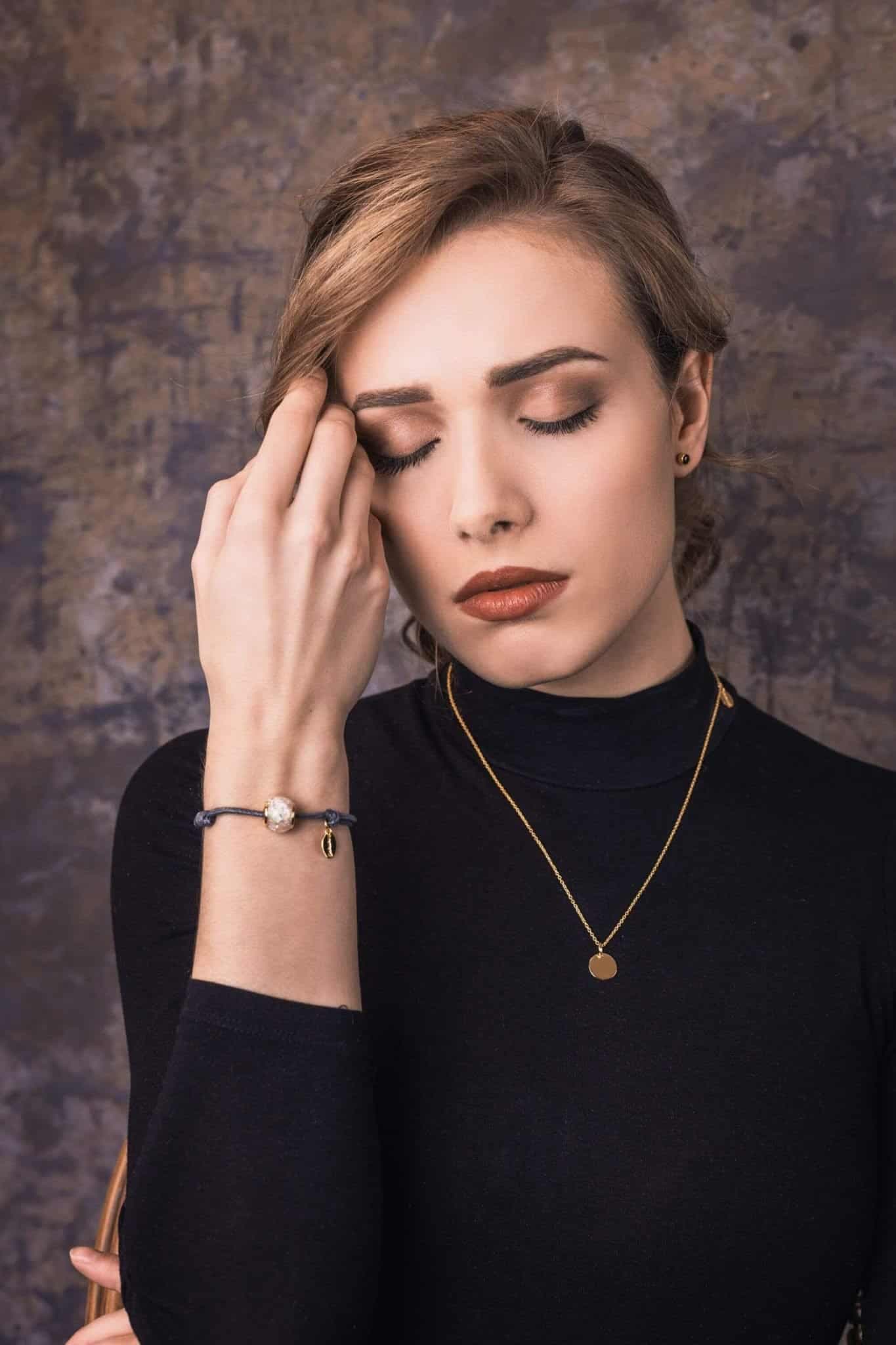 Goldene Halskette mit einem runden Anhänger und einem blauen Kordelarmband mit einer runden, marmorierten Perle und goldenem Anhänger.