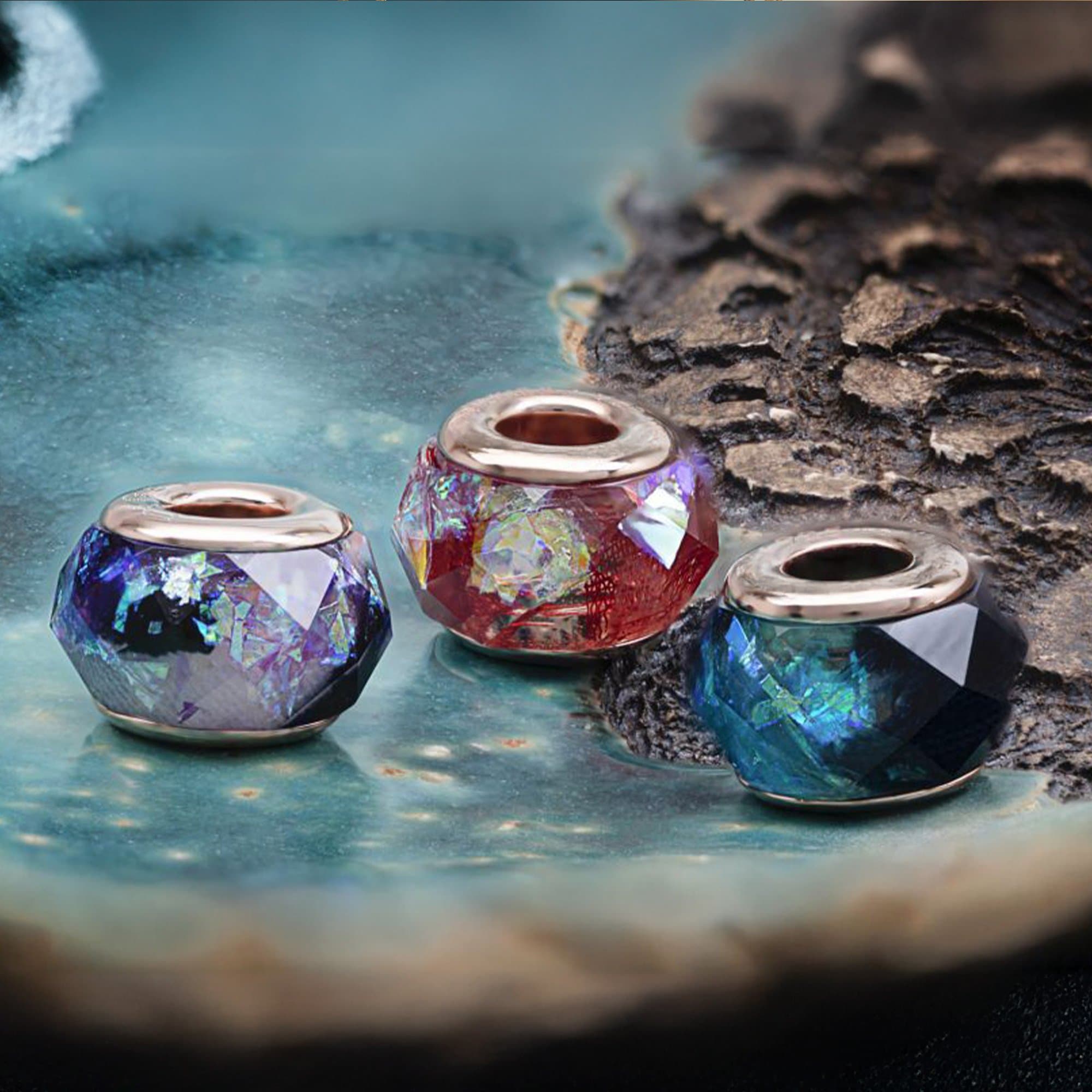 Drei facettierte Glasperlen mit roségoldenen Kappen in blauen, roten und blaugrünen Farbtönen.
