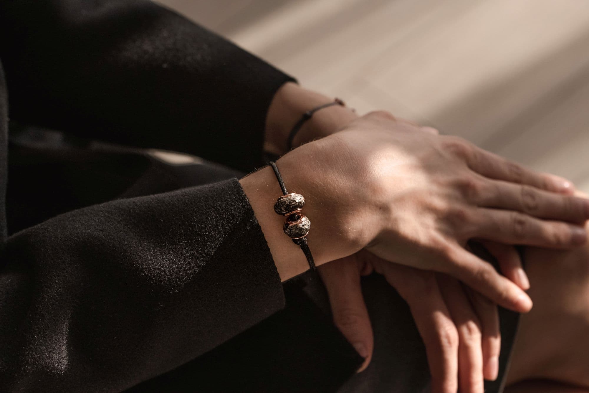 Schwarzes Kordelarmband mit zwei strukturierten silbernen Perlen und roségoldenen Akzenten.
