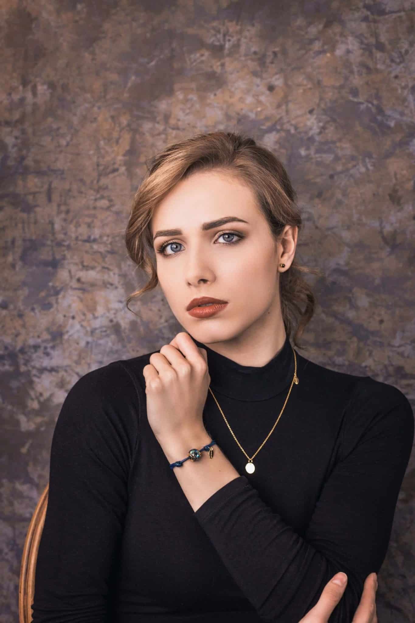 Blaues Kordelarmband mit einer runden, blauen, gesprenkelten Perle und einem goldenen Anhänger.