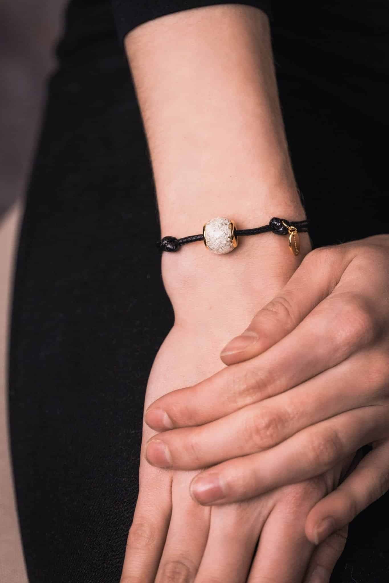 Schwarzes Kordelarmband mit einer weißen gesprenkelten Perle und einem goldenen Akzent.