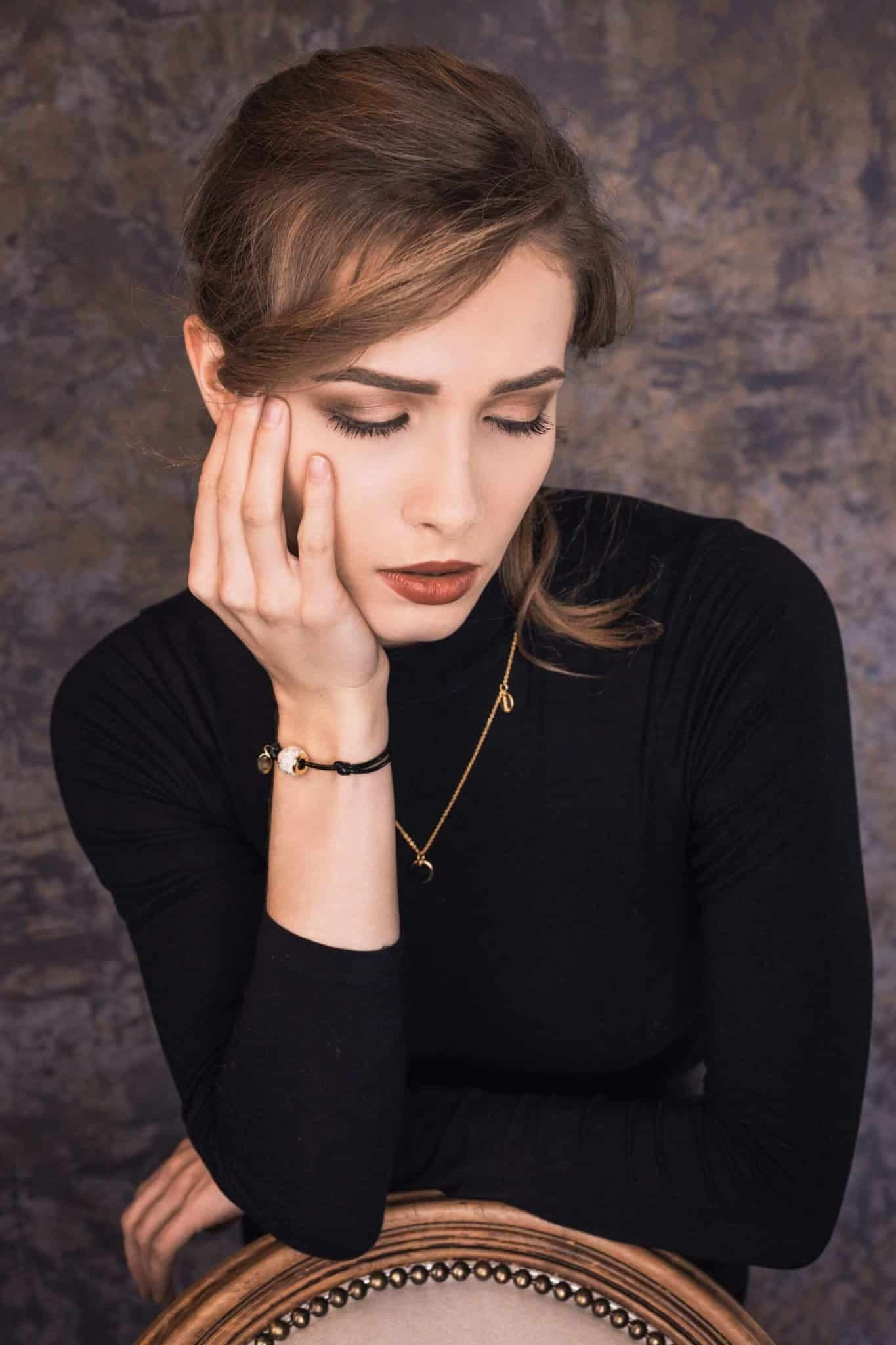 Goldhalskette mit Halbmondanhänger und schwarzes Kordelarmband mit einer weißen Perle und einem Goldanhänger.