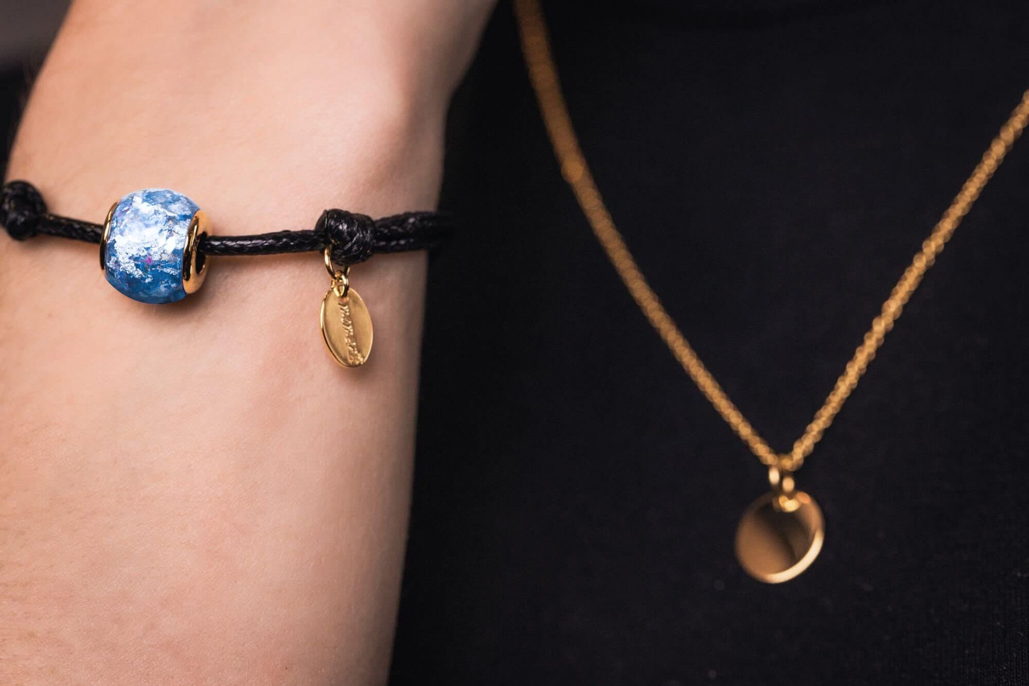 Blau und weiß marmorierte Perle mit goldenen Akzenten an einem schwarzen Kordelarmband.