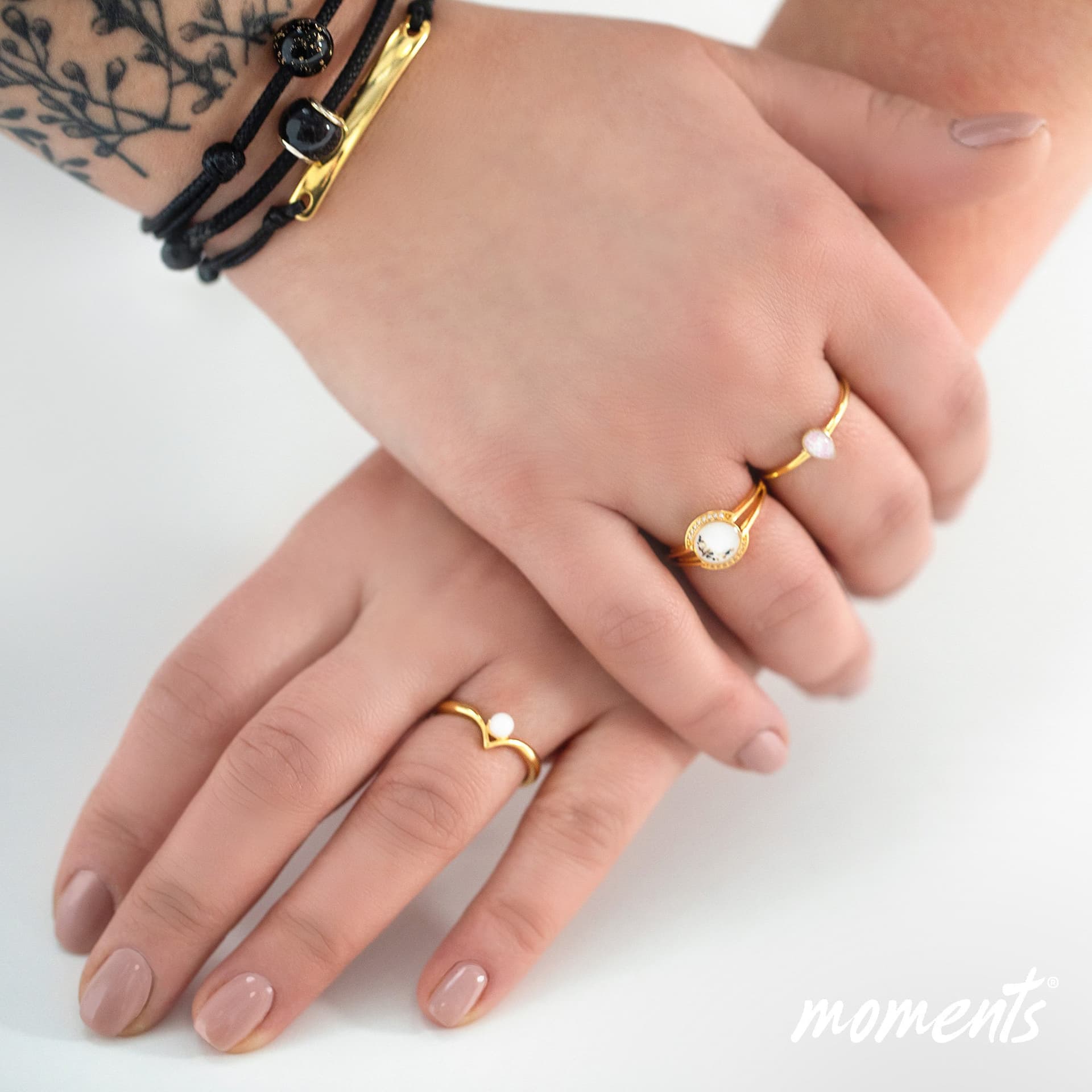 Guldring med en hvid, oval sten og sorte pletter og en gylden chevron-ring med en hvid perle.
