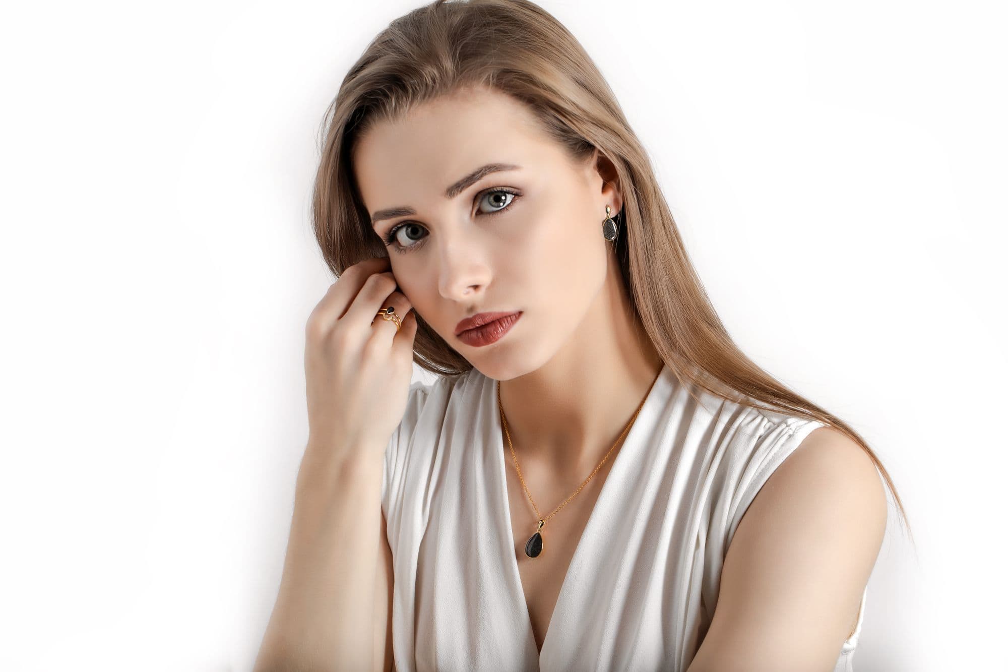 Goldhalskette mit einem schwarzen, tropfenförmigen Anhänger, Goldring mit einem schwarzen Stein und schwarze, tropfenförmige Ohrringe.