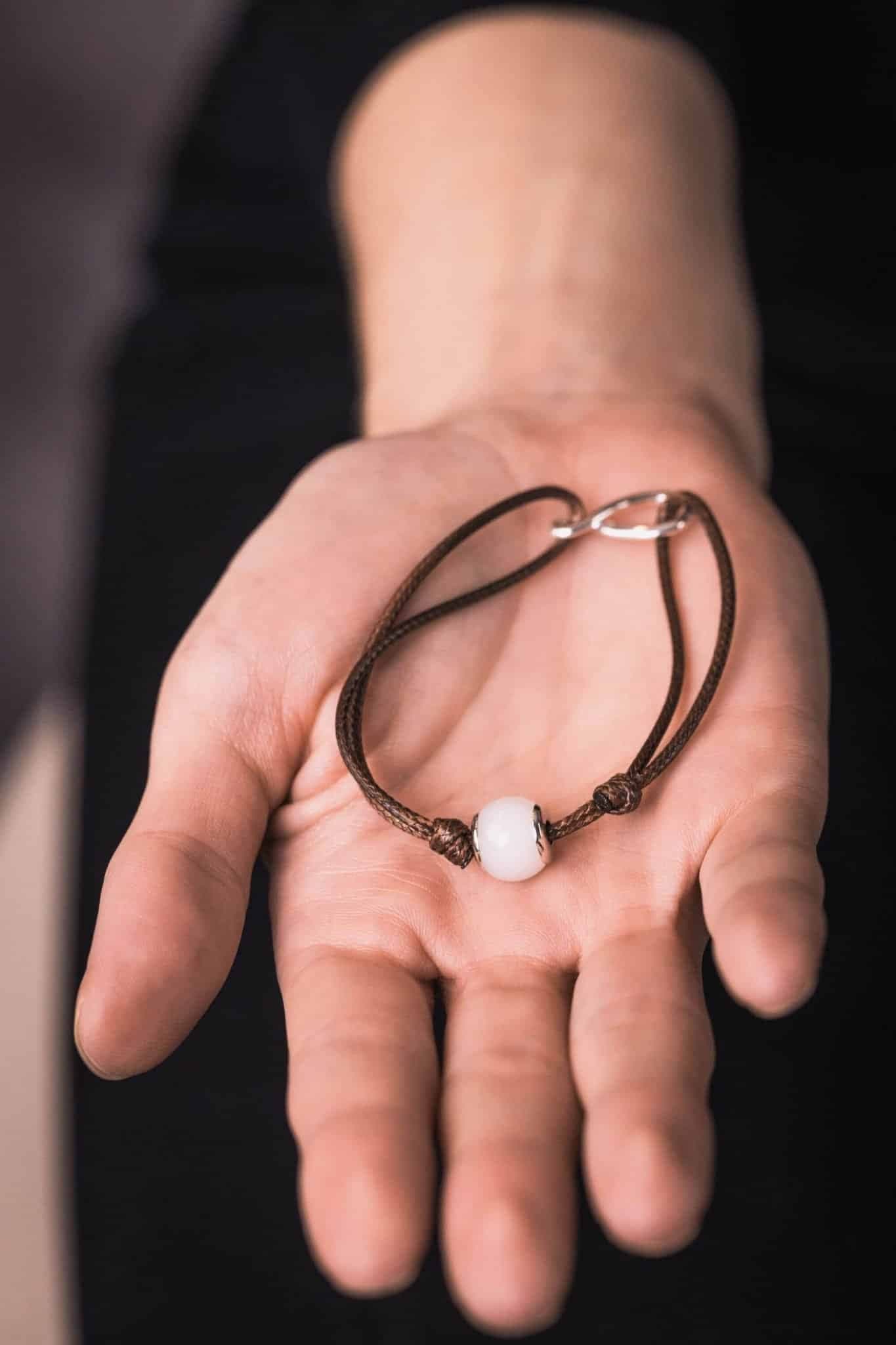 Braunes Kordelarmband mit einer weißen Perle und silbernem Verschluss.