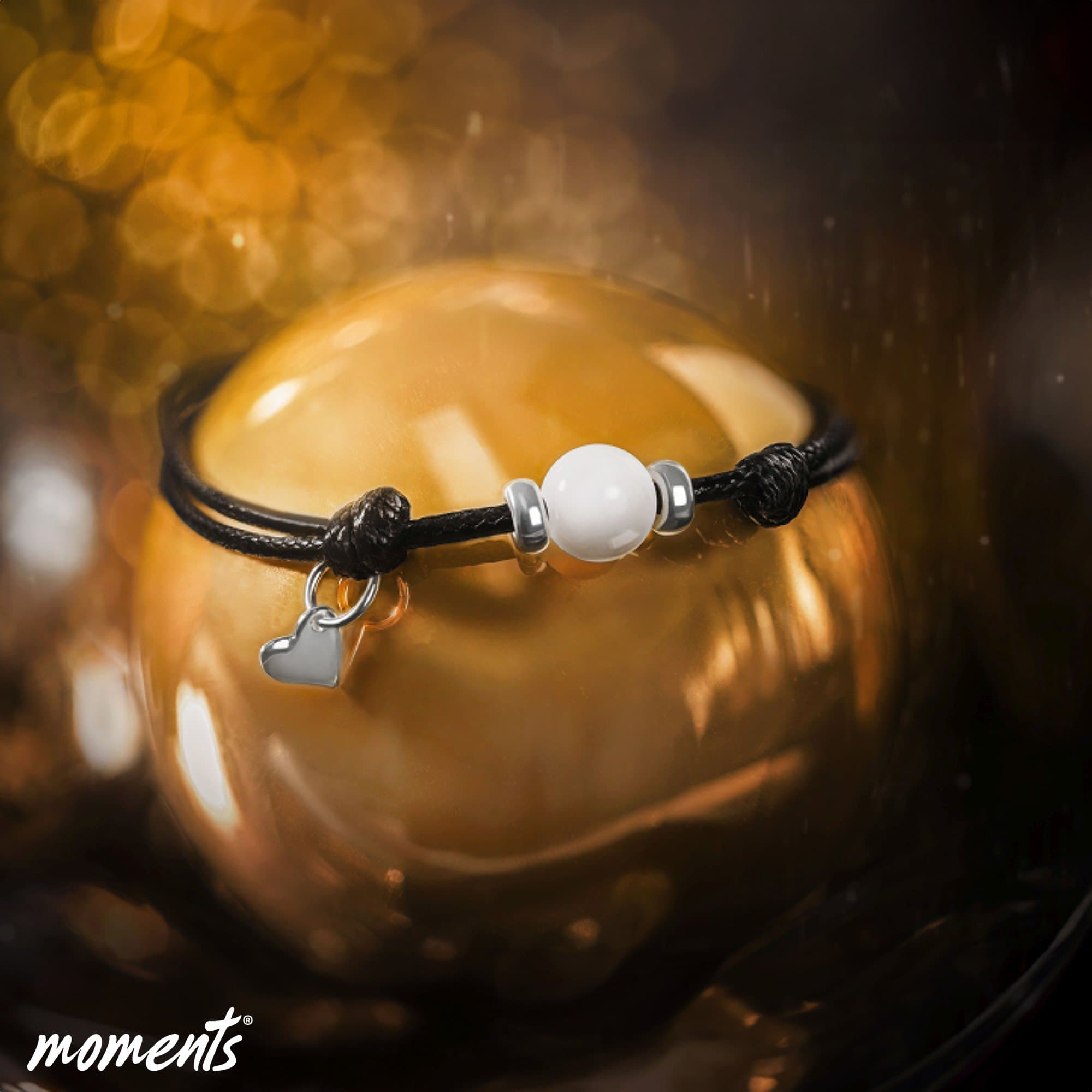Schwarzes Kordelarmband mit einer weißen Perle, silbernen Abstandshaltern und einem silbernen Herzanhänger.