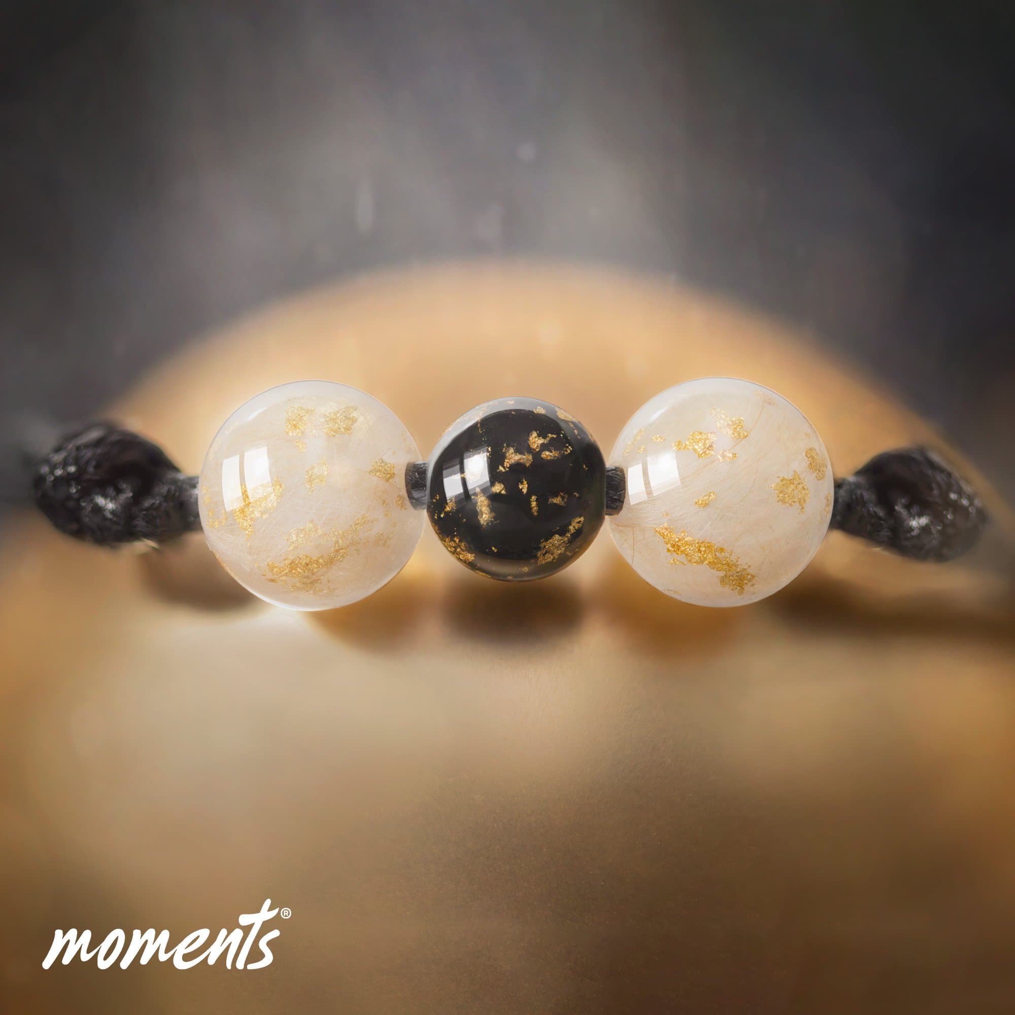 Perlenarmband mit zwei durchscheinenden weißen Perlen mit goldenen Sprenkeln und einer schwarzen Perle.