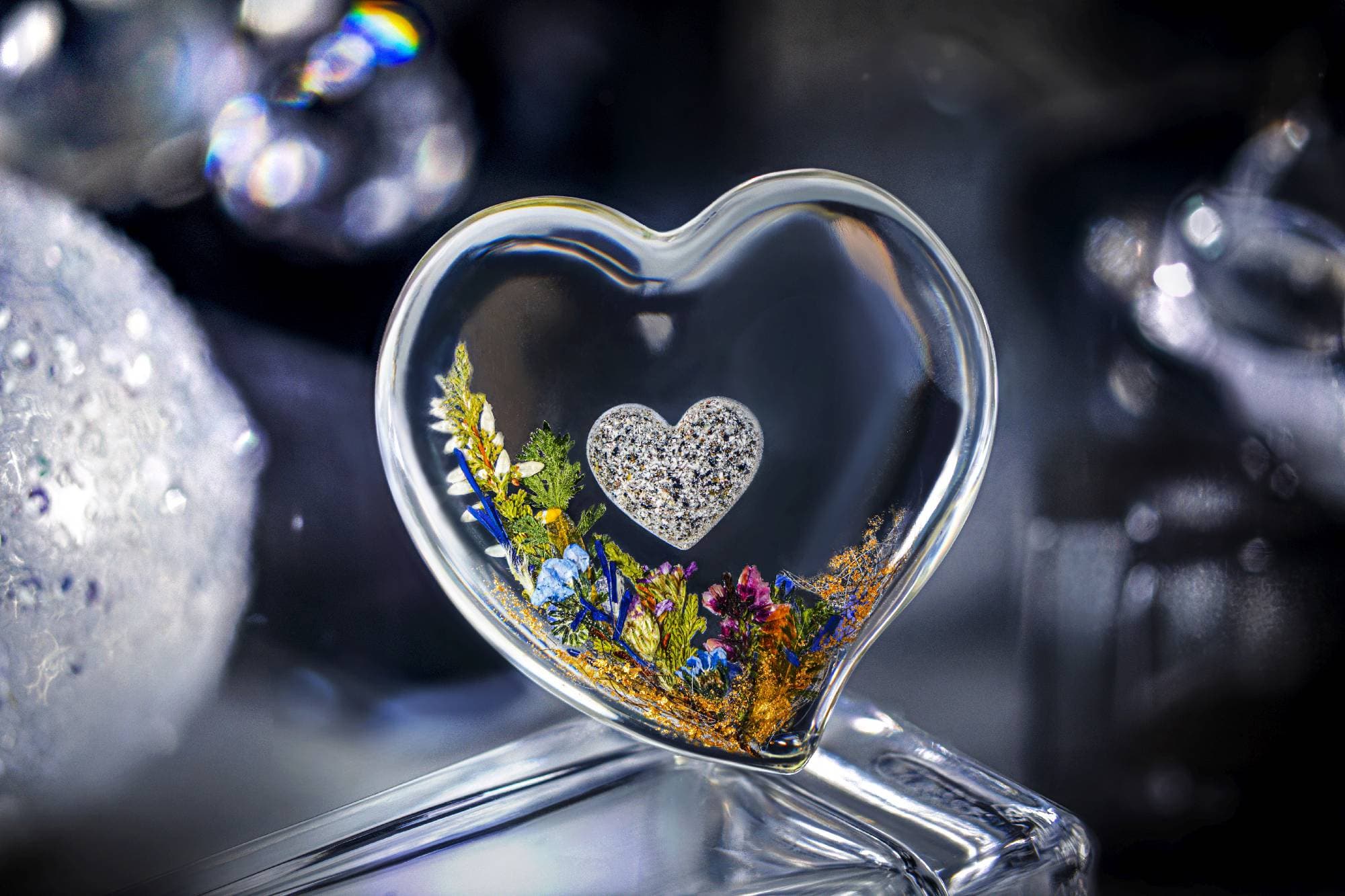 Klares herzförmiges Glas mit getrockneten Blumen, Goldflocken und einem kleinen, strukturierten Herzanhänger.